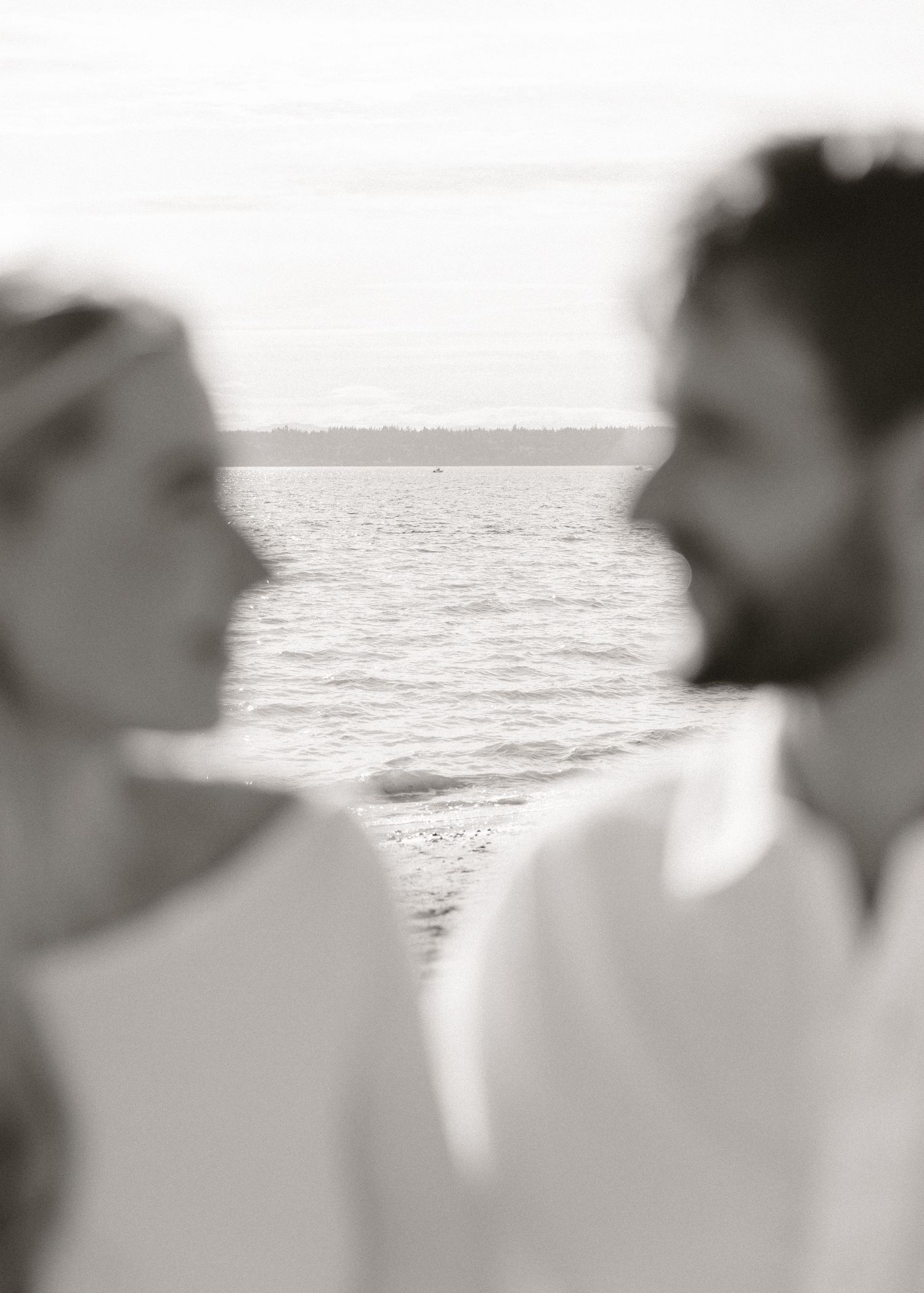 Black and white photo of a couple facing each other with a serene ocean horizon in the soft-focus background.