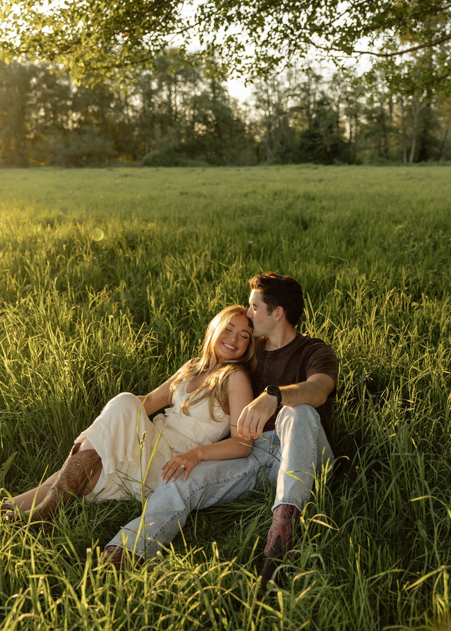 Couple relaxing together in tall green grass field, bathed in warm sunset light.