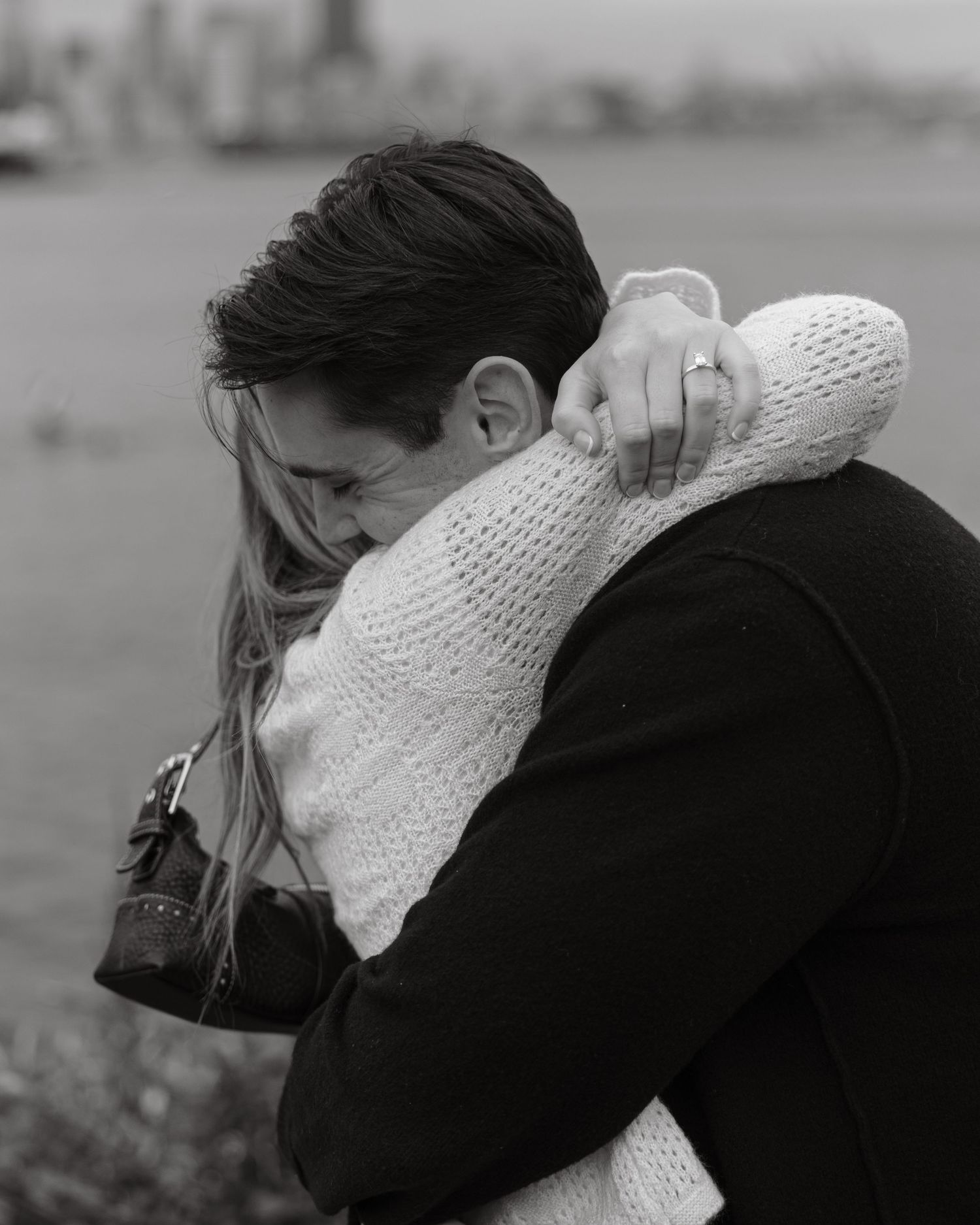 A tender embrace captured in black and white with a waterfront cityscape in the background.