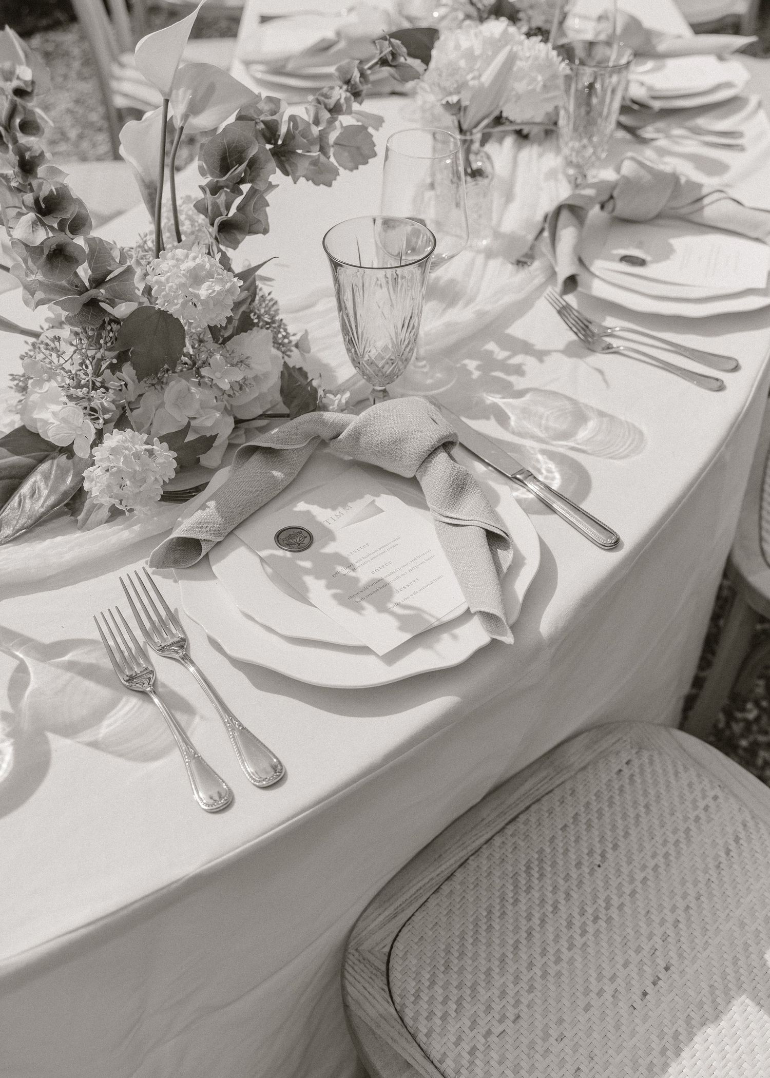 Black and white wedding reception table with floral centerpieces, crystal glasses, silver cutlery, and menu cards.