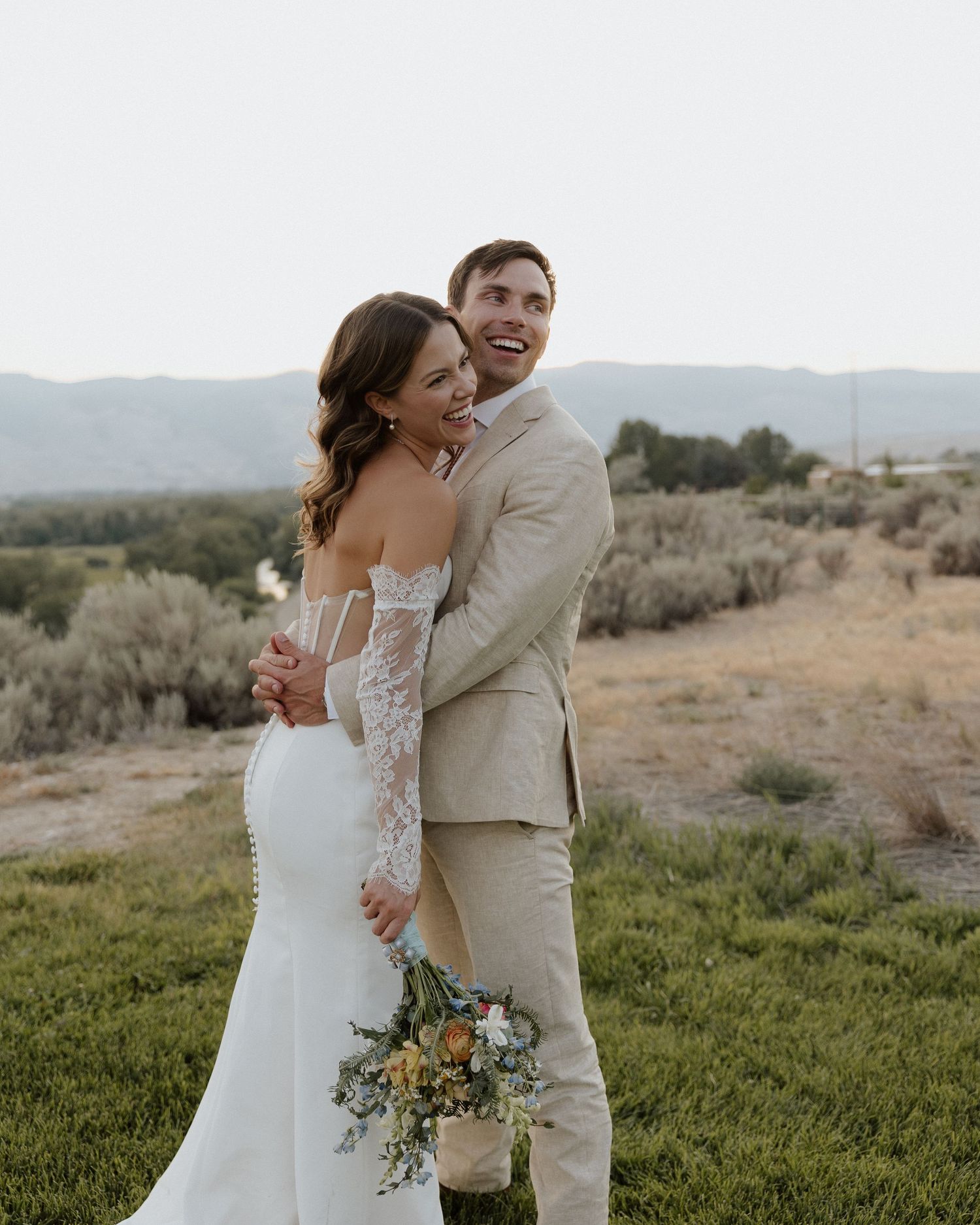 Joyful couple embrace in outdoor setting with mountains and desert landscape.