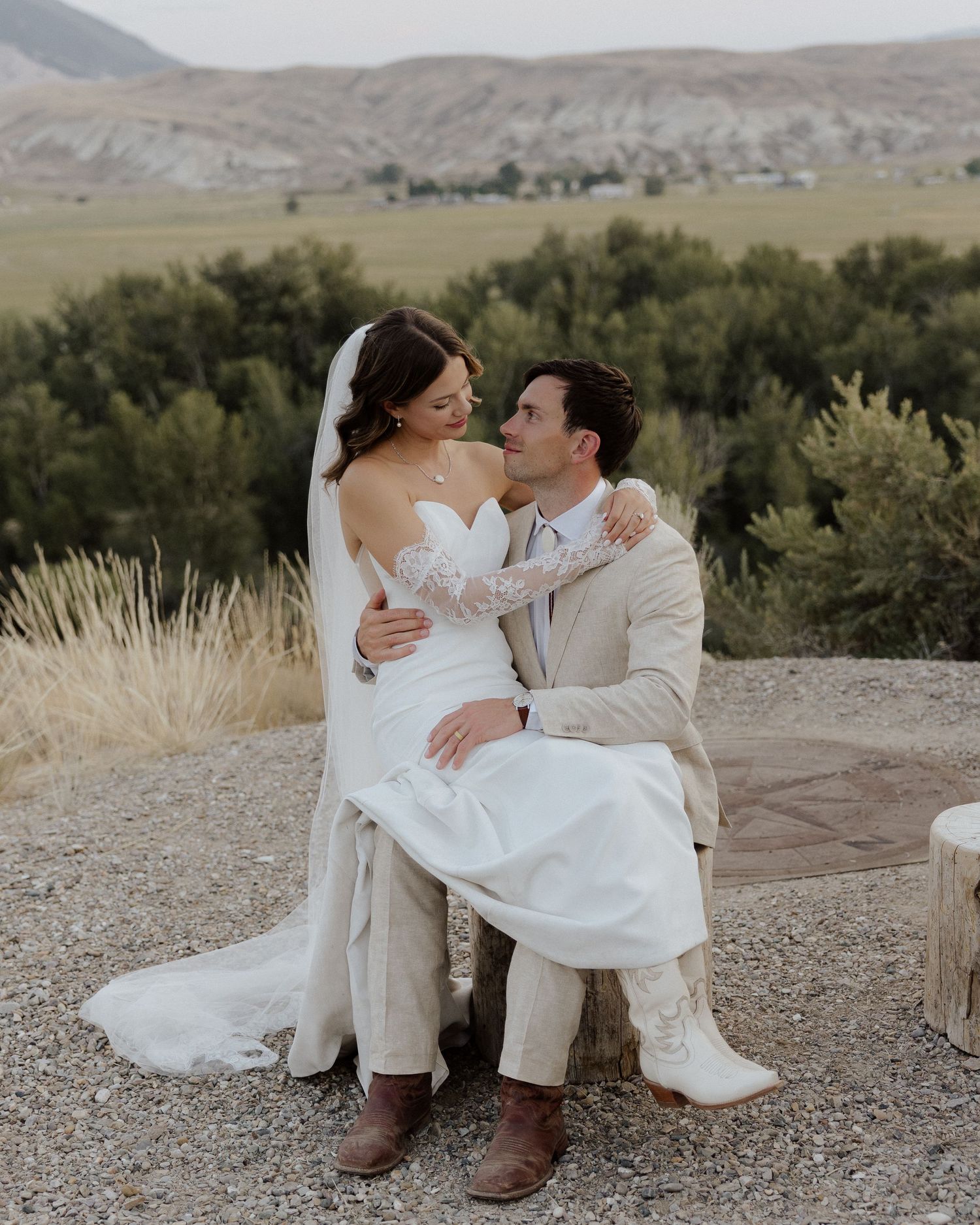 Intimate moment between newlyweds sitting on rustic log bench with scenic mountain views.