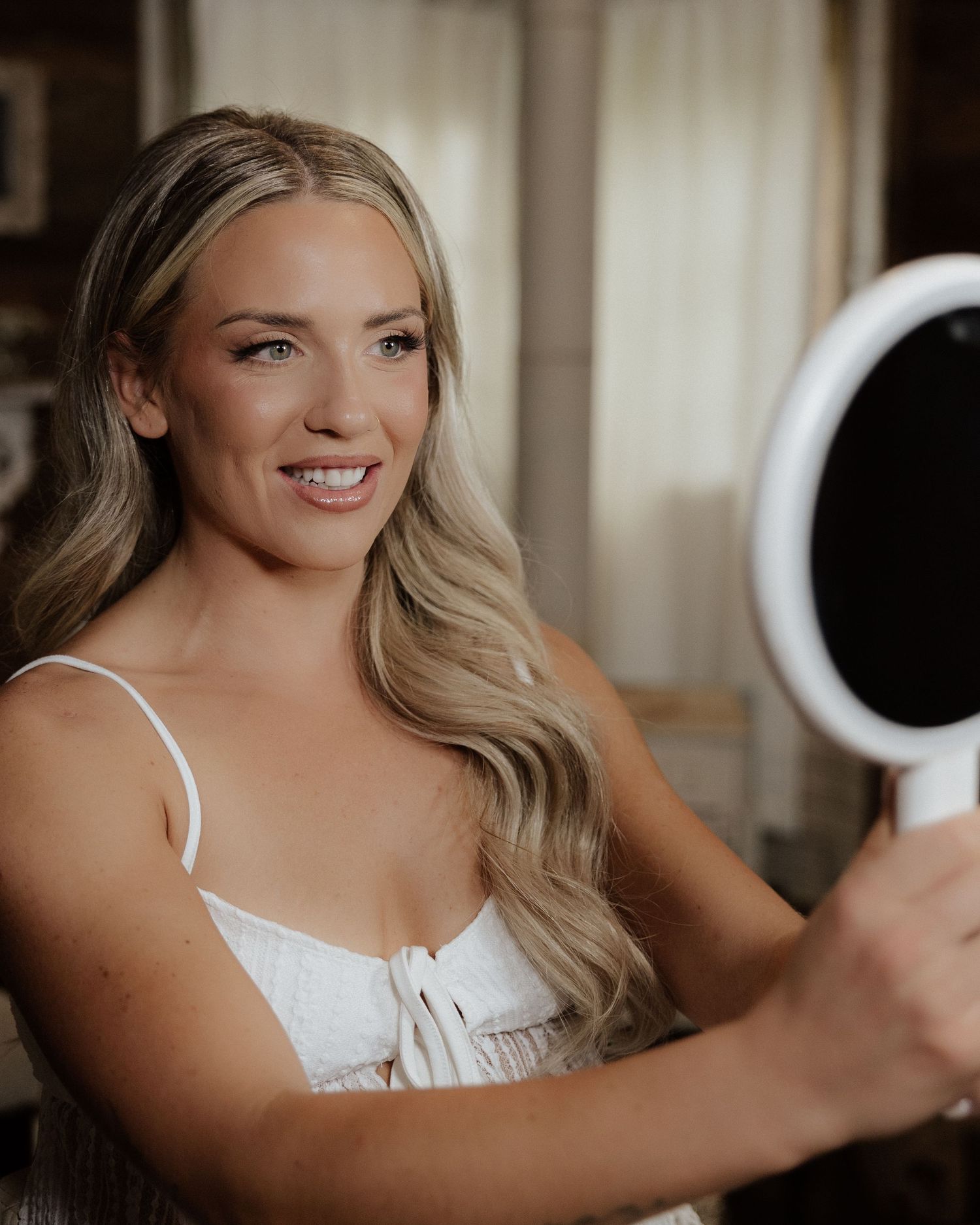 A woman in white getting ready in a softly lit room.