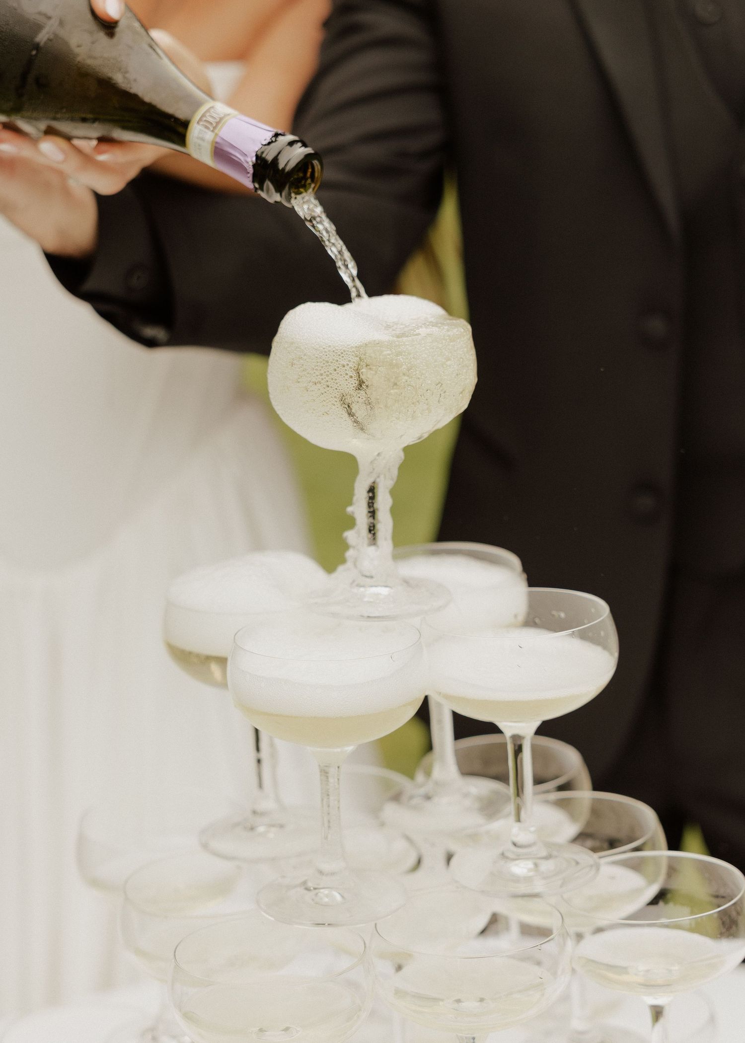 Champagne being poured into a tower of coupe glasses at a wedding reception celebration.