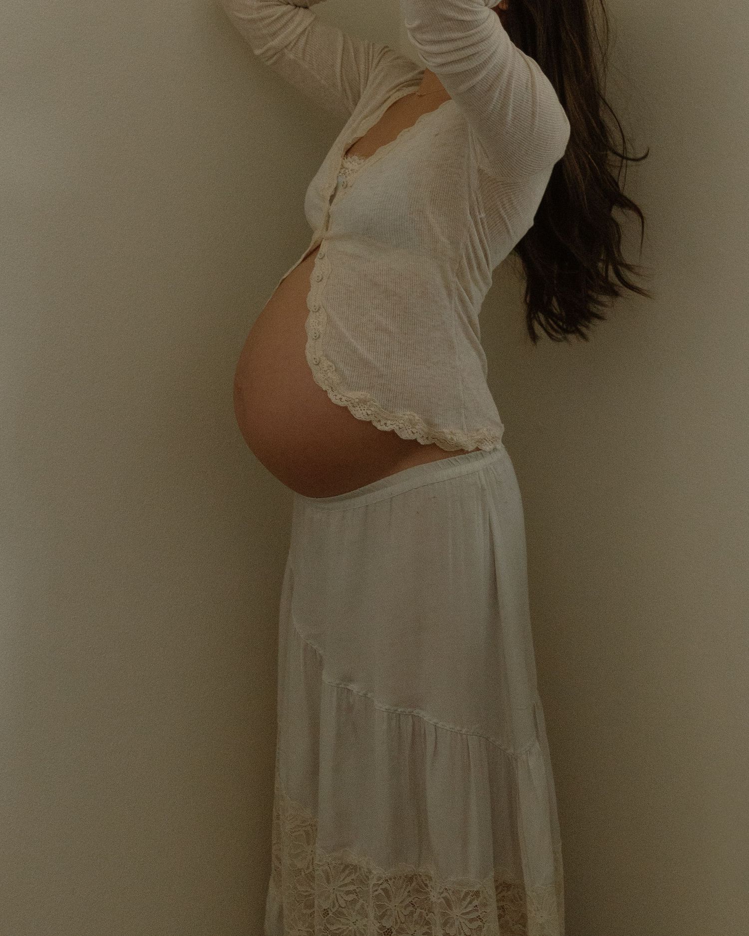 A silhouette of a pregnant woman in white lace dress showing her baby bump.