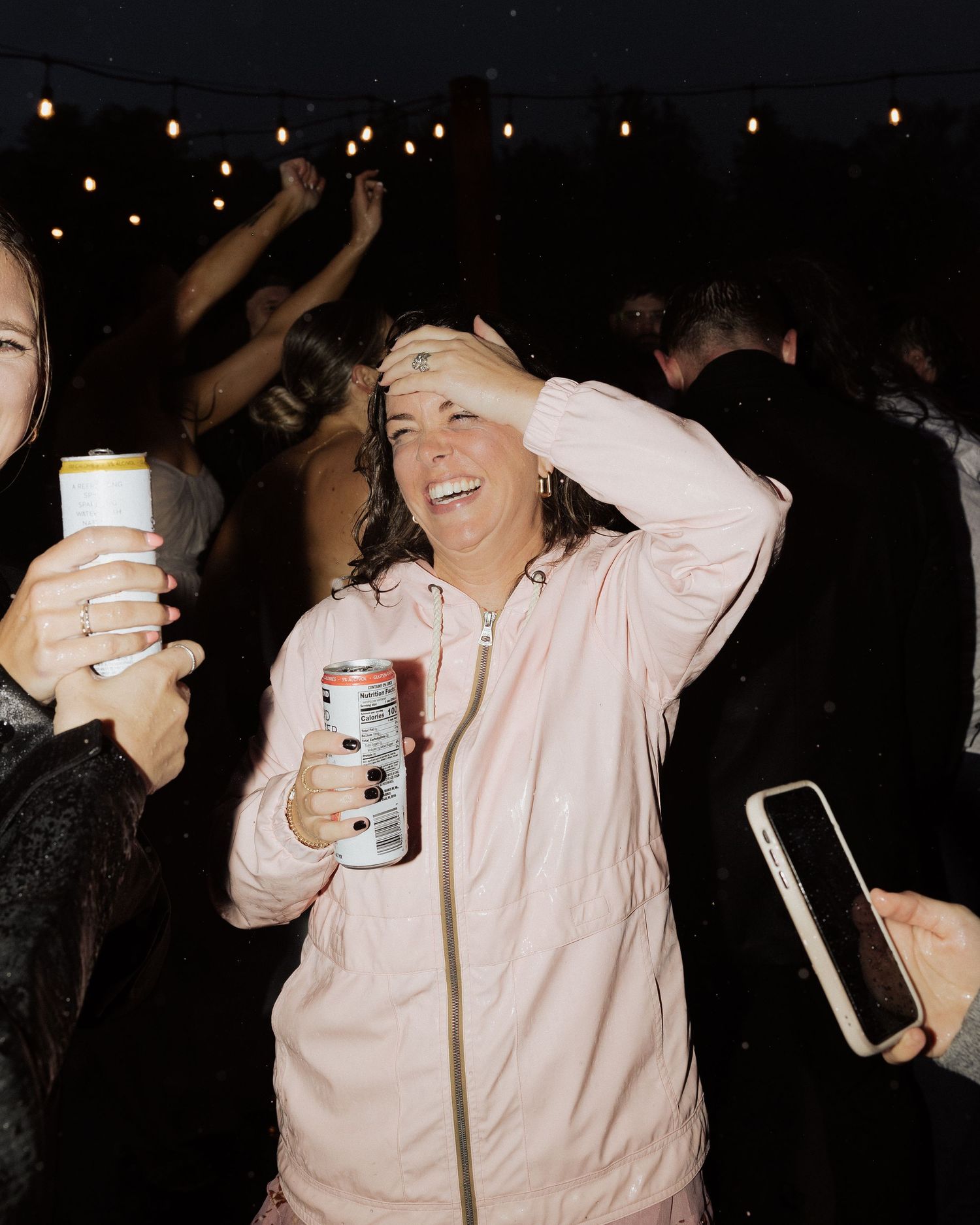 Party guests enjoying drinks and dancing under outdoor string lights at night.