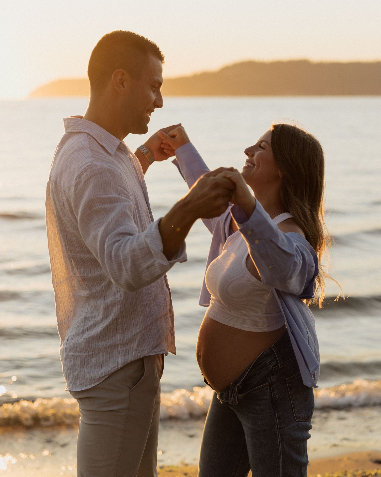 Expecting couple sharing a tender moment at sunset by the ocean.