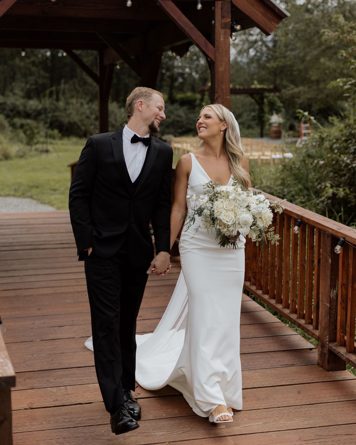 Newlyweds walking hand in hand on wooden deck surrounded by nature.