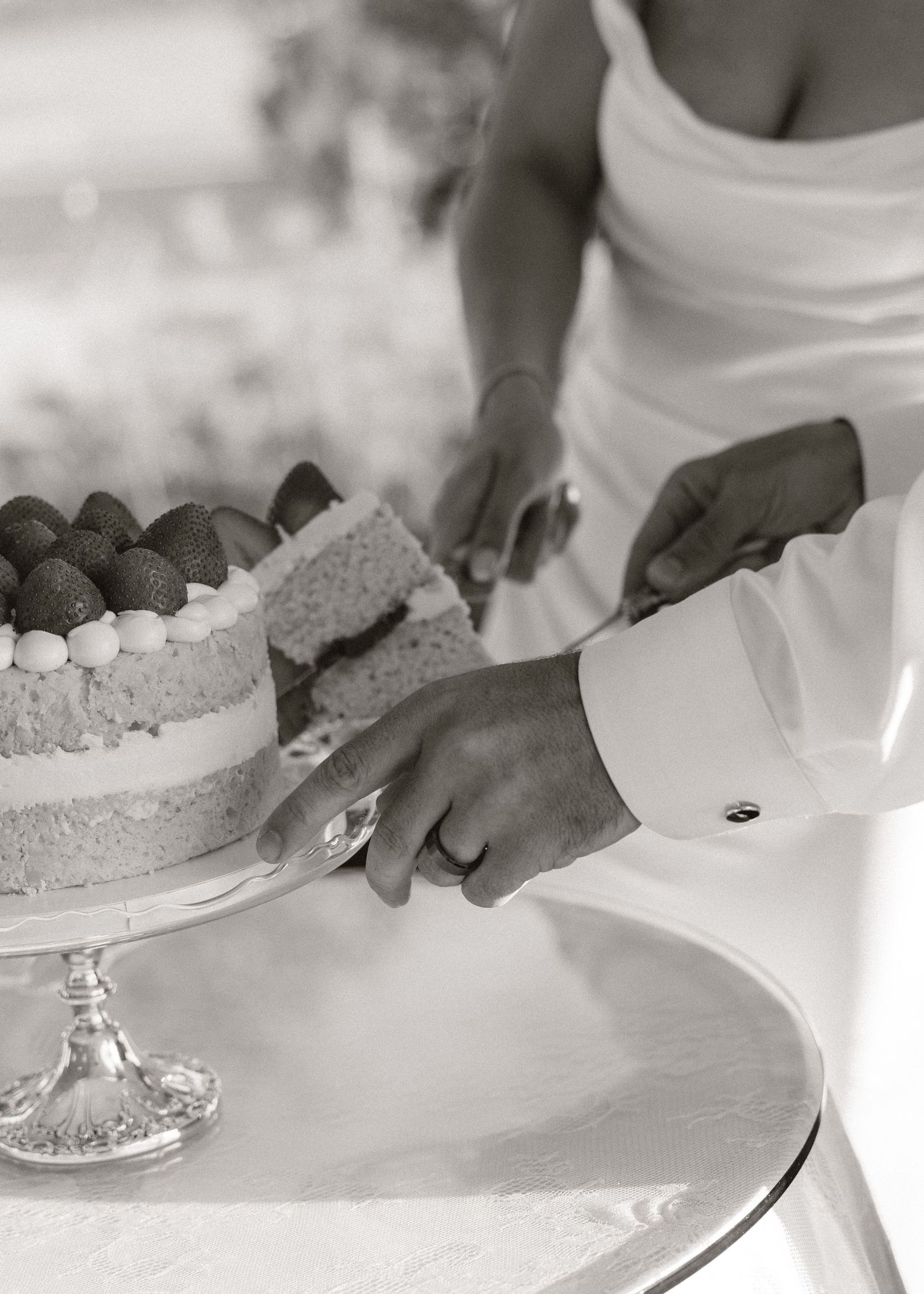 Bride and groom cut naked wedding cake topped with fresh strawberries in black and white photo.