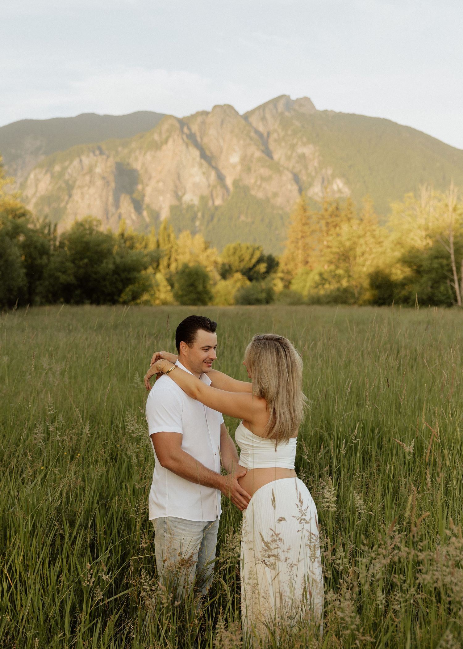 Couple holding hands in a green meadow with a mountain backdrop during golden hour.