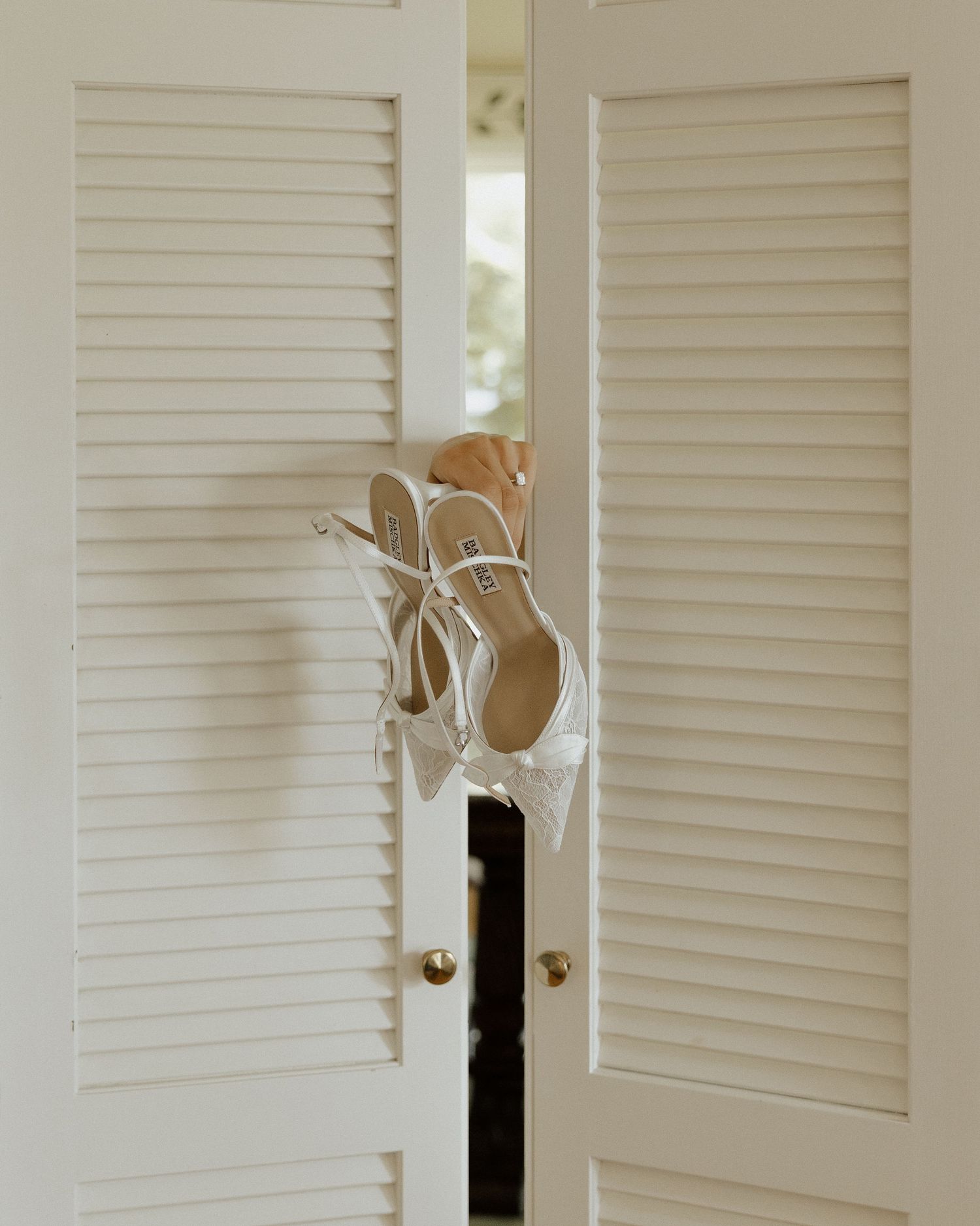 White strappy heels hanging on louvered closet doors, perfect bridal shoes for a wedding day.