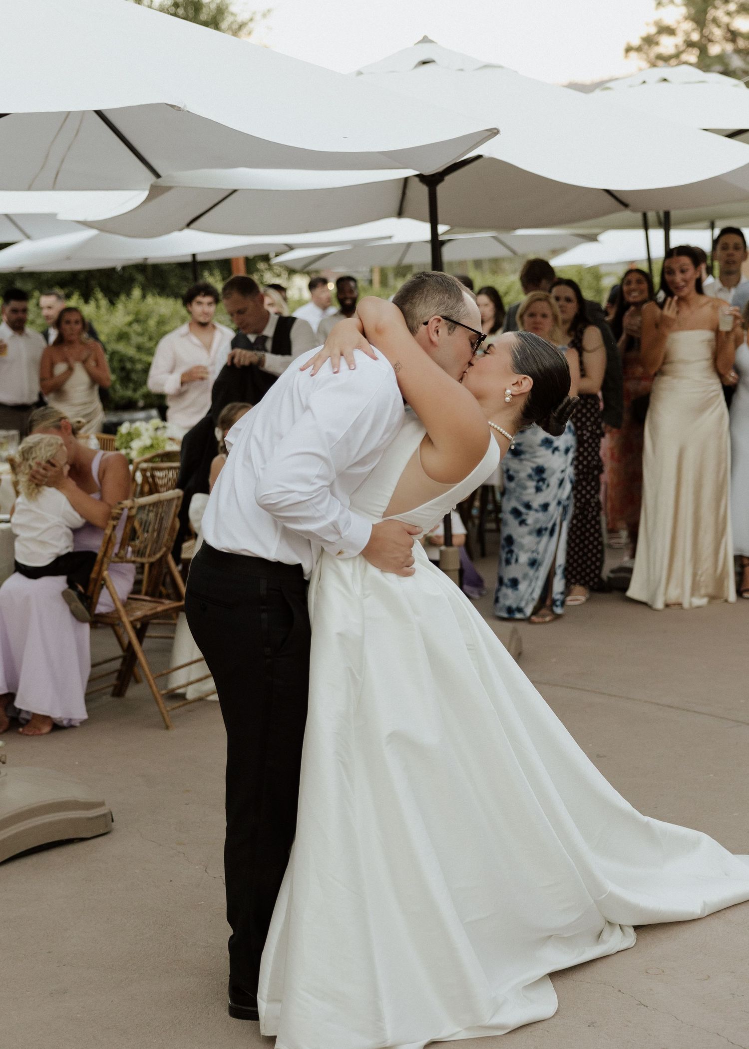 Groom dipping bride for a romantic kiss on the dance floor surrounded by wedding guests.