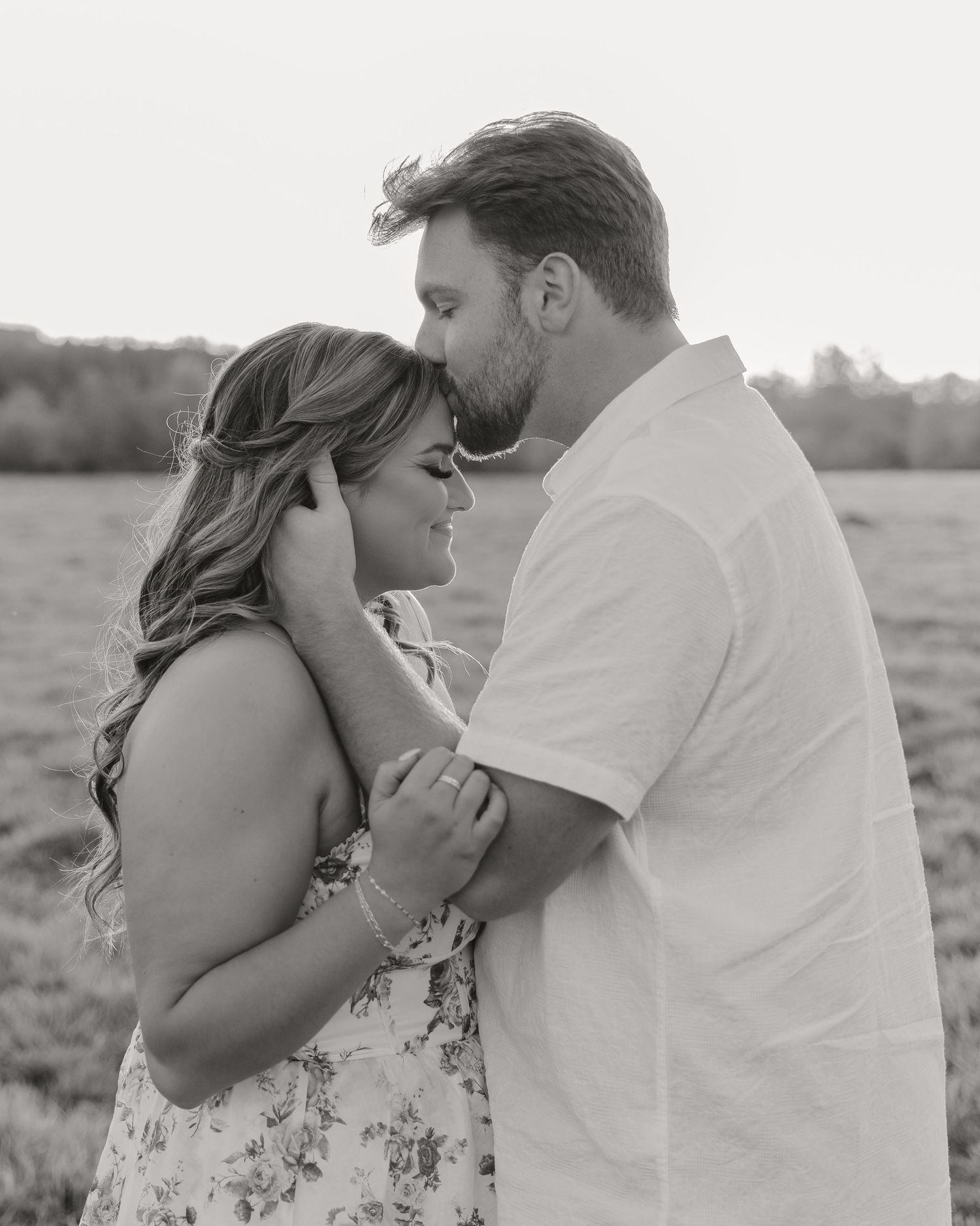 Intimate black and white portrait of couple embracing in field.
