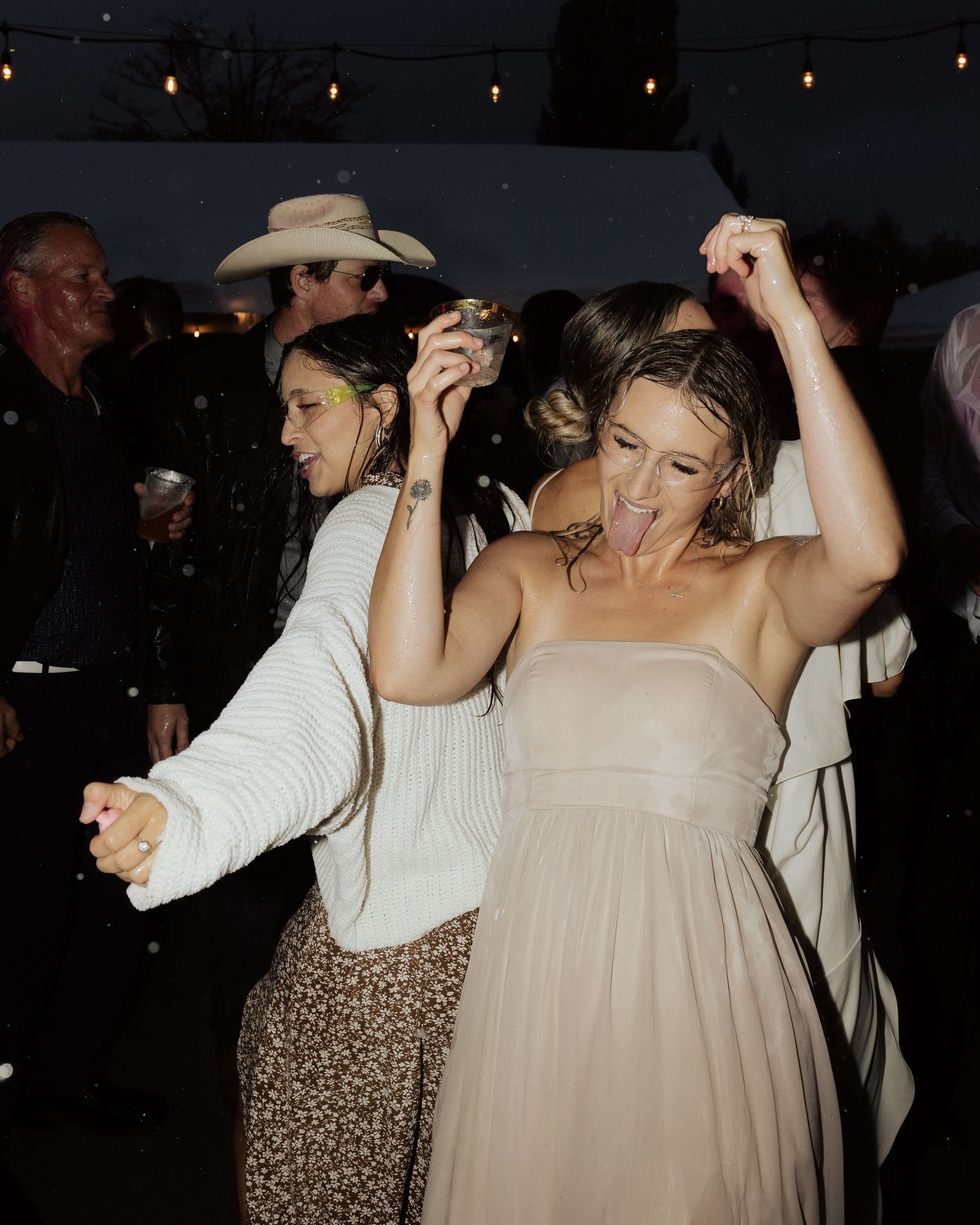 Two people dancing enthusiastically at an outdoor party under string lights.