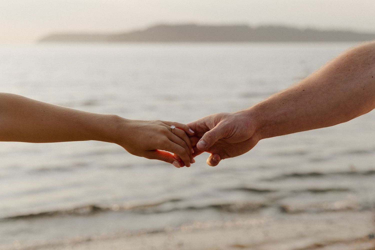Close-up of two hands joining together against an ocean sunset backdrop.