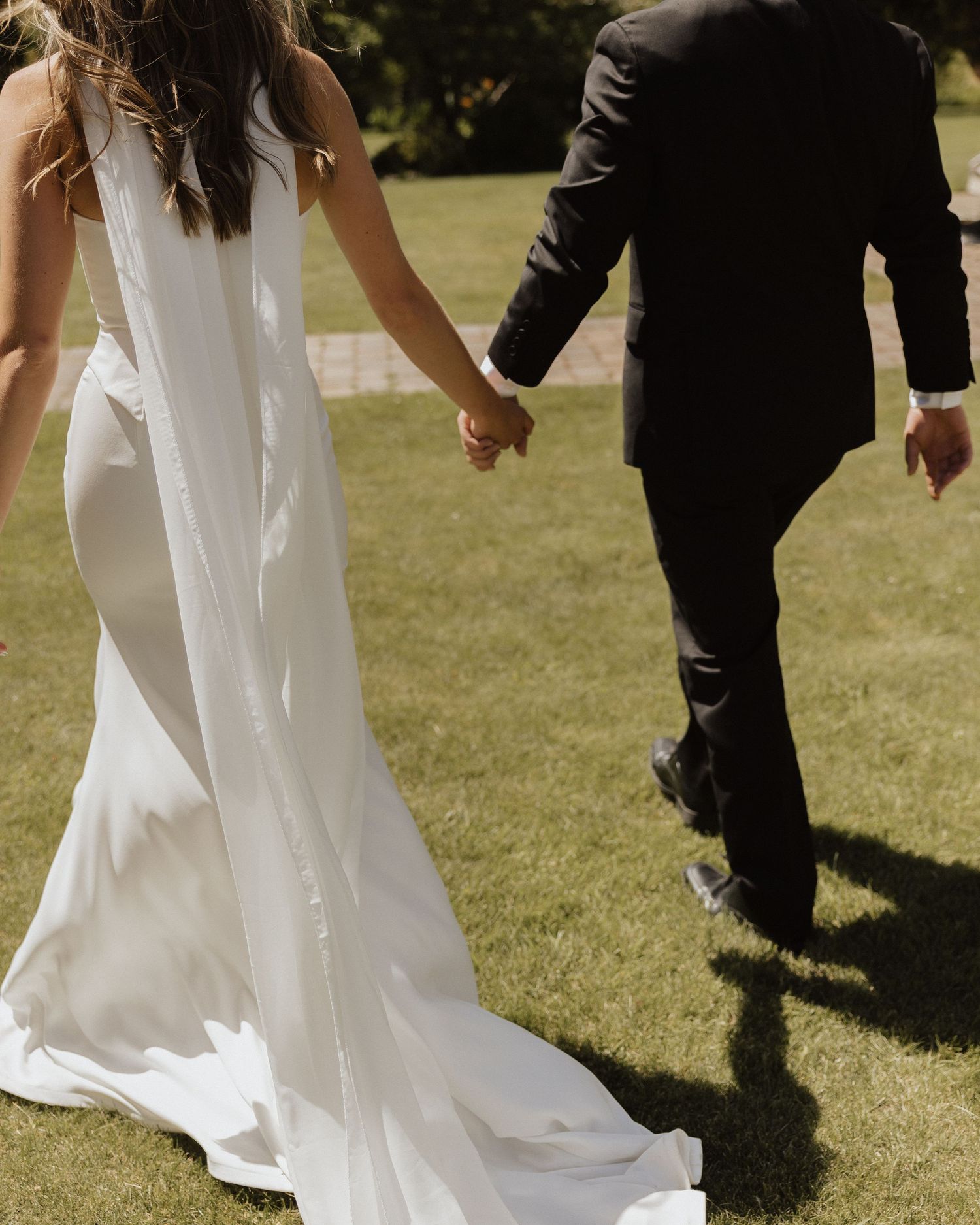 White wedding gowns and black tuxedos creating an elegant contrast as the wedding party walks on grass.