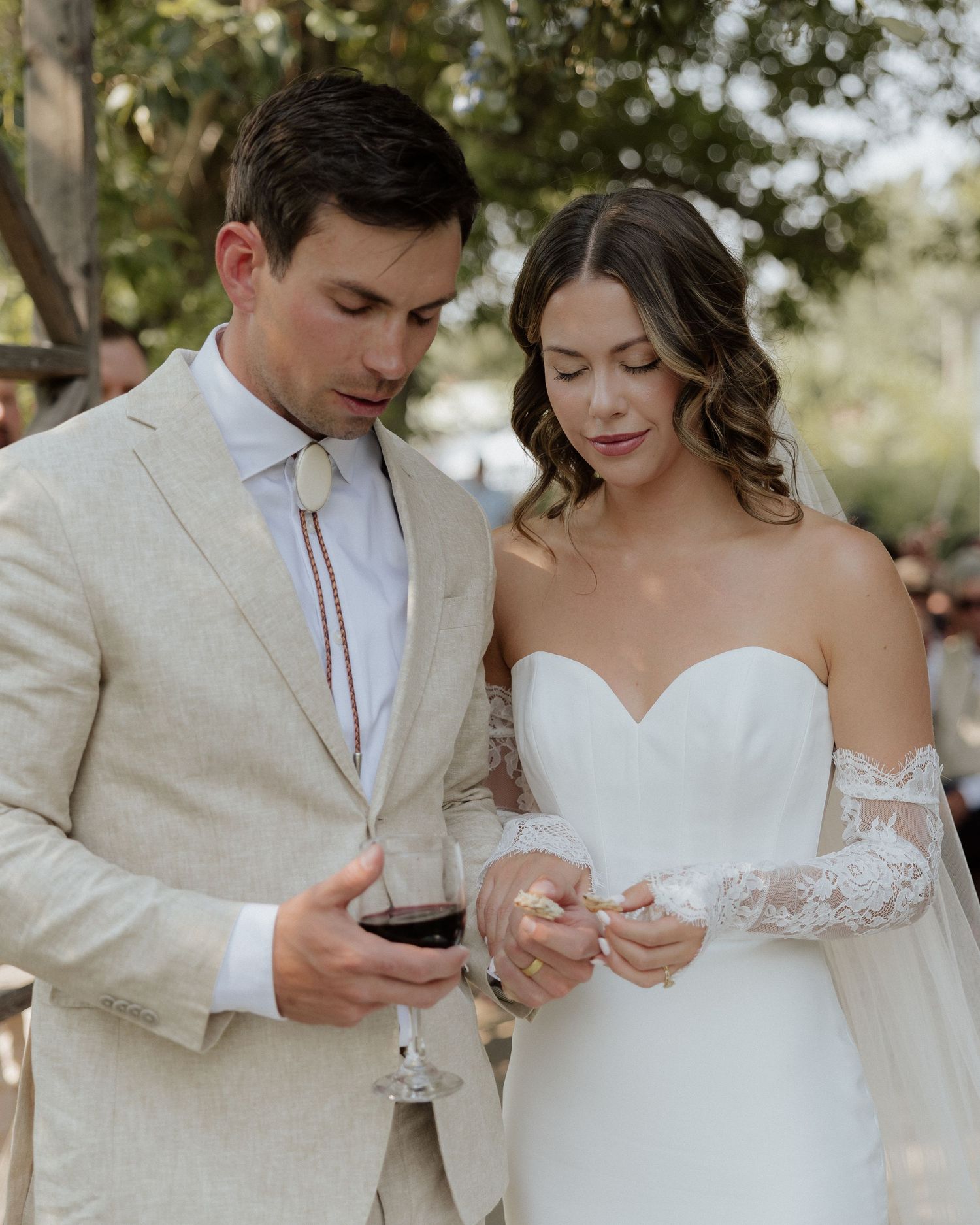 Couple in wedding attire checking their phones during outdoor ceremony.
