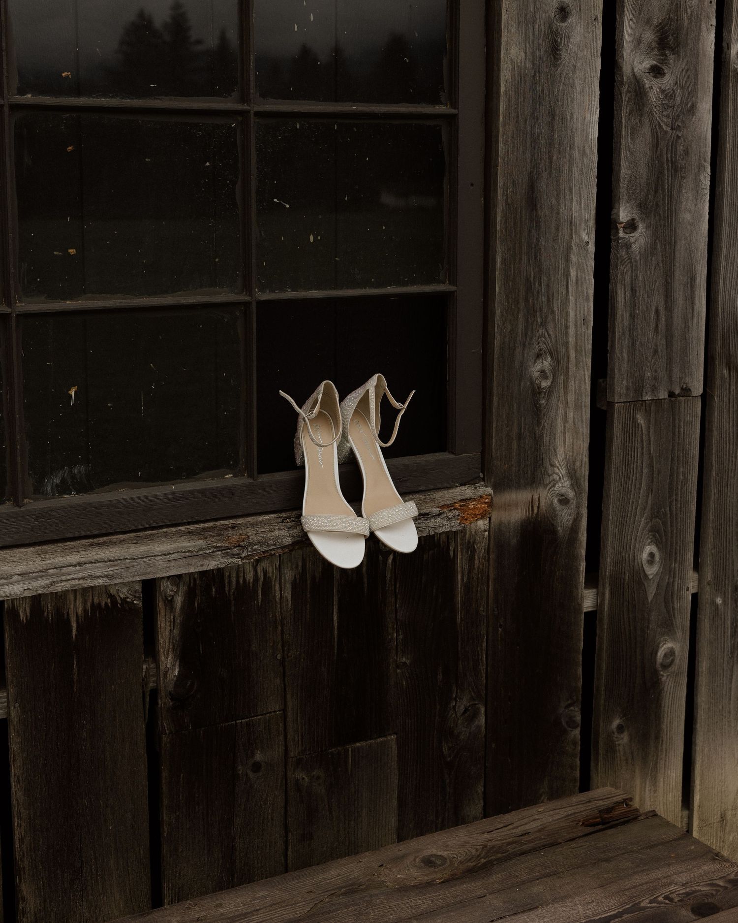 White bridal sandals displayed on rustic wooden window ledge.