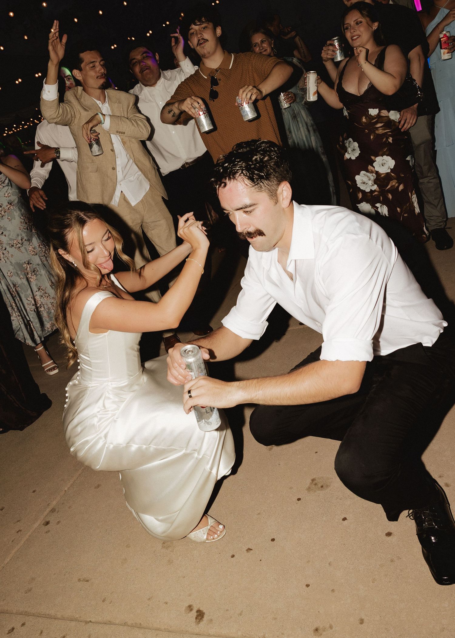 Bride and groom dancing energetically with guests at lively outdoor wedding reception at night.