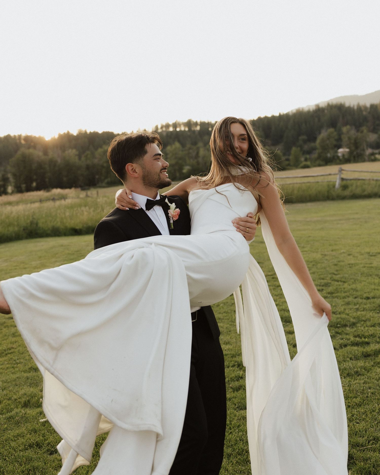 Bride and groom dance outdoors in a green field at sunset with flowing white wedding dress movement.