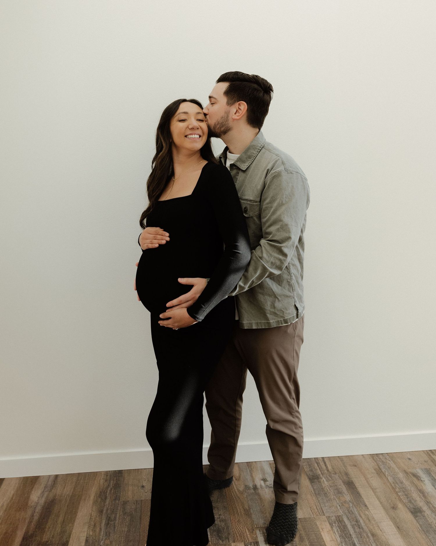 Intimate maternity photo of couple laughing together against neutral background.