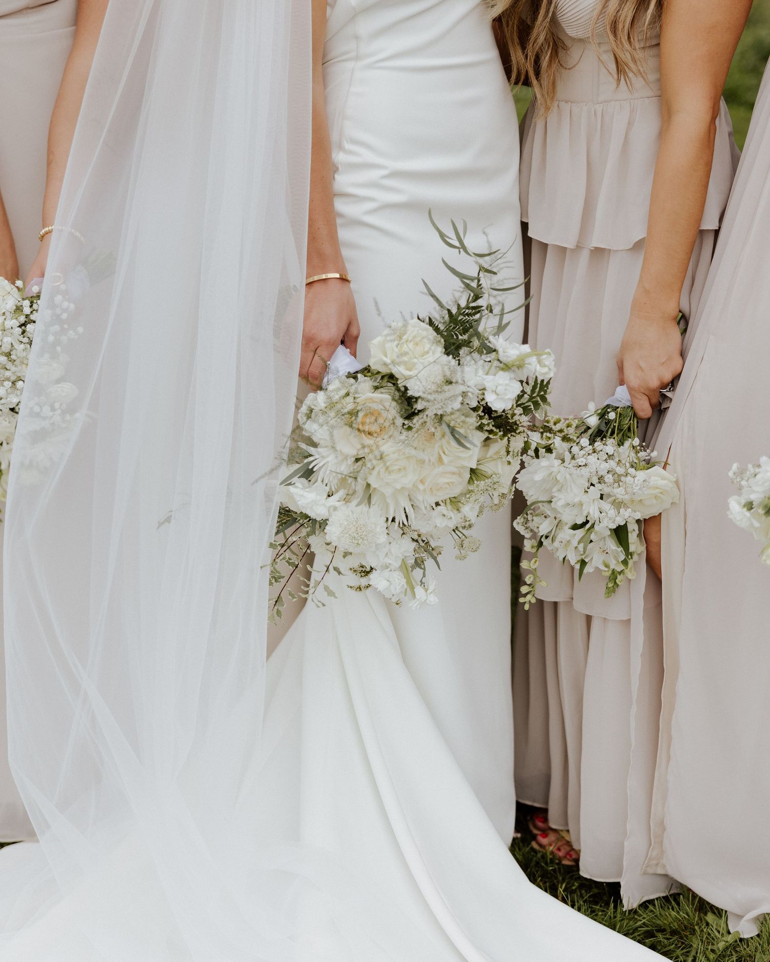 Close-up of elegant white wedding bouquets held against neutral bridesmaid dresses.