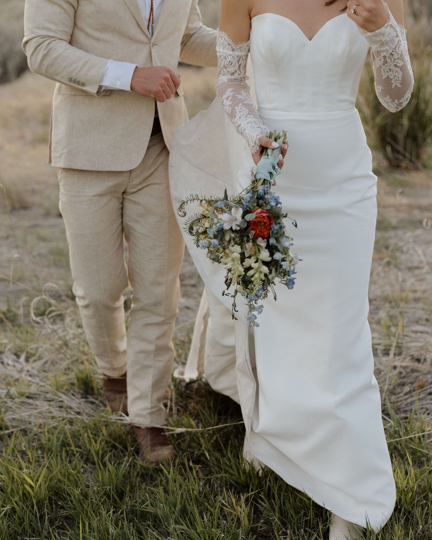 Close-up of bride and groom's attire showing white dress, beige suit, and colorful bouquet.