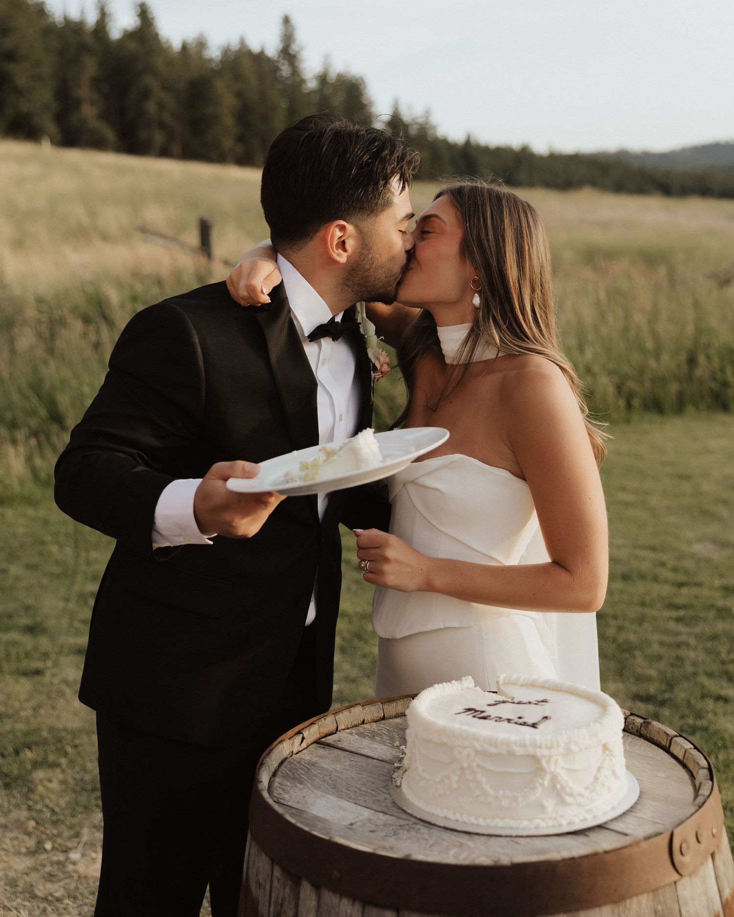 Newlyweds share intimate moment while feeding each other wedding cake outdoors.