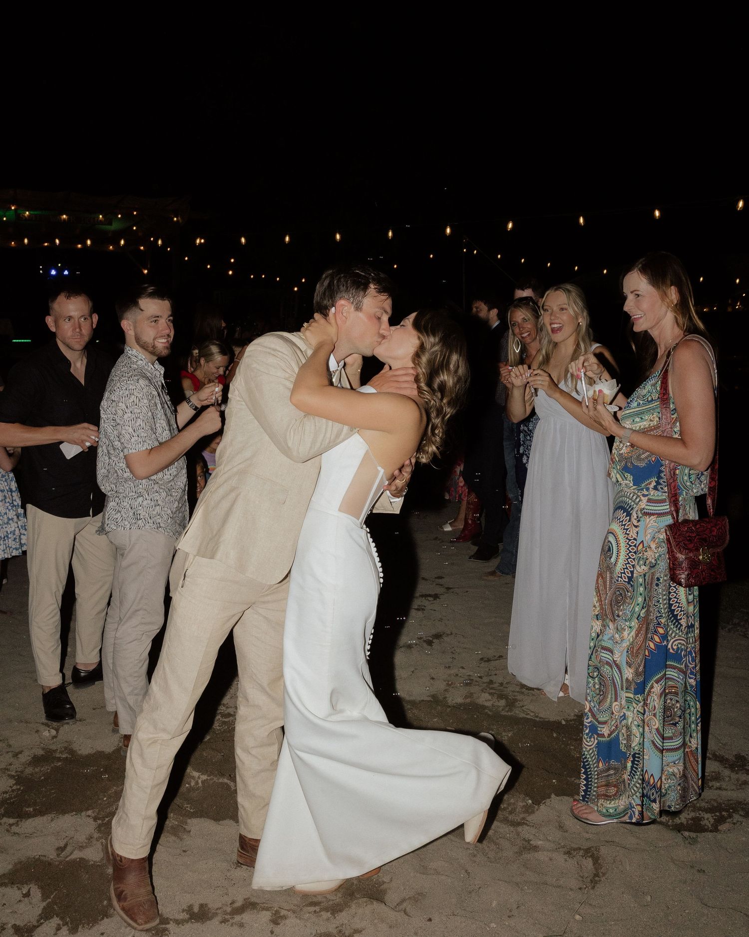 Romantic dance moment at beach wedding reception surrounded by guests at night.