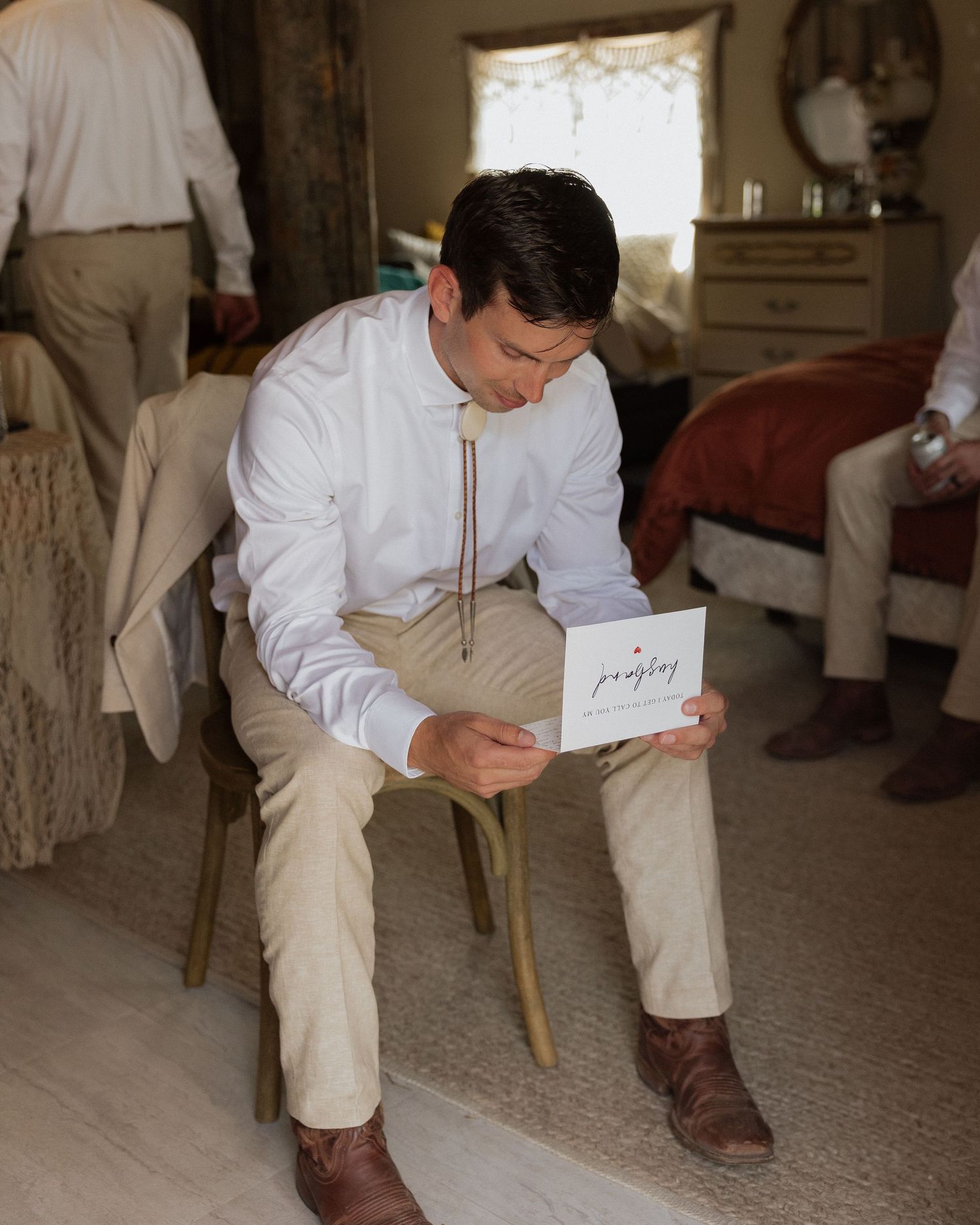 Person in white dress shirt and khakis reading from a small card while seated.