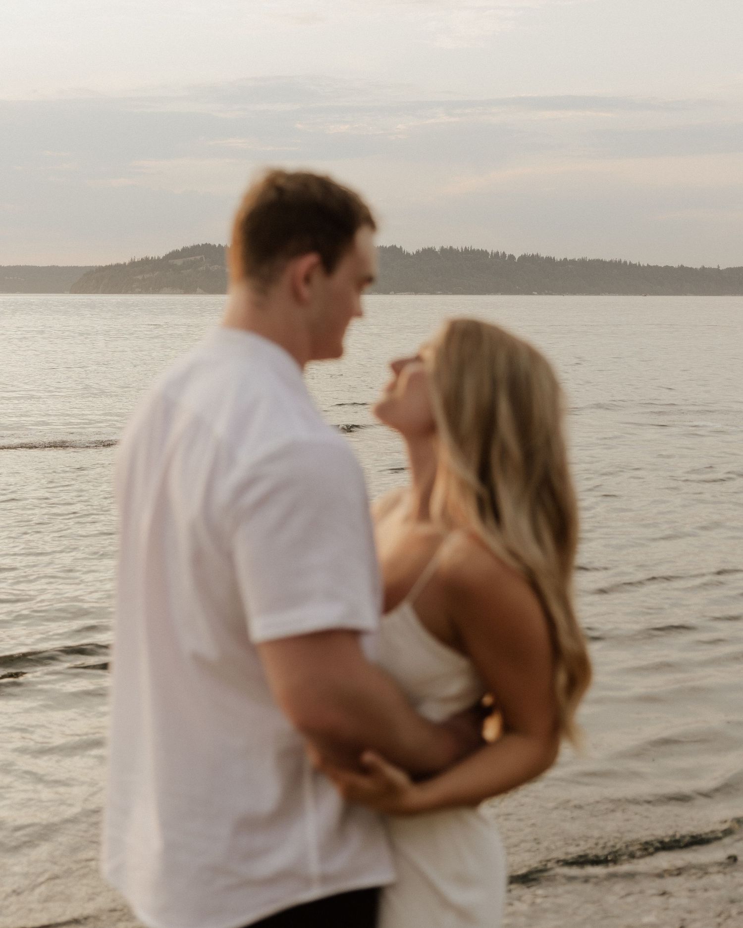 Couple in casual white attire sharing intimate moment by waterfront at dusk.