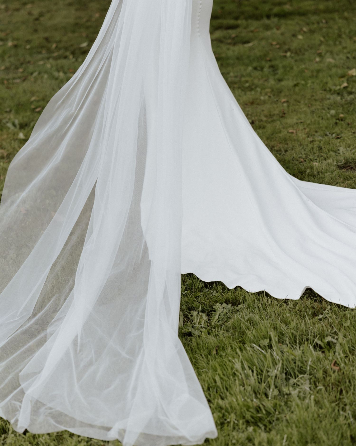 Flowing white wedding dress train and veil spread across green grass.