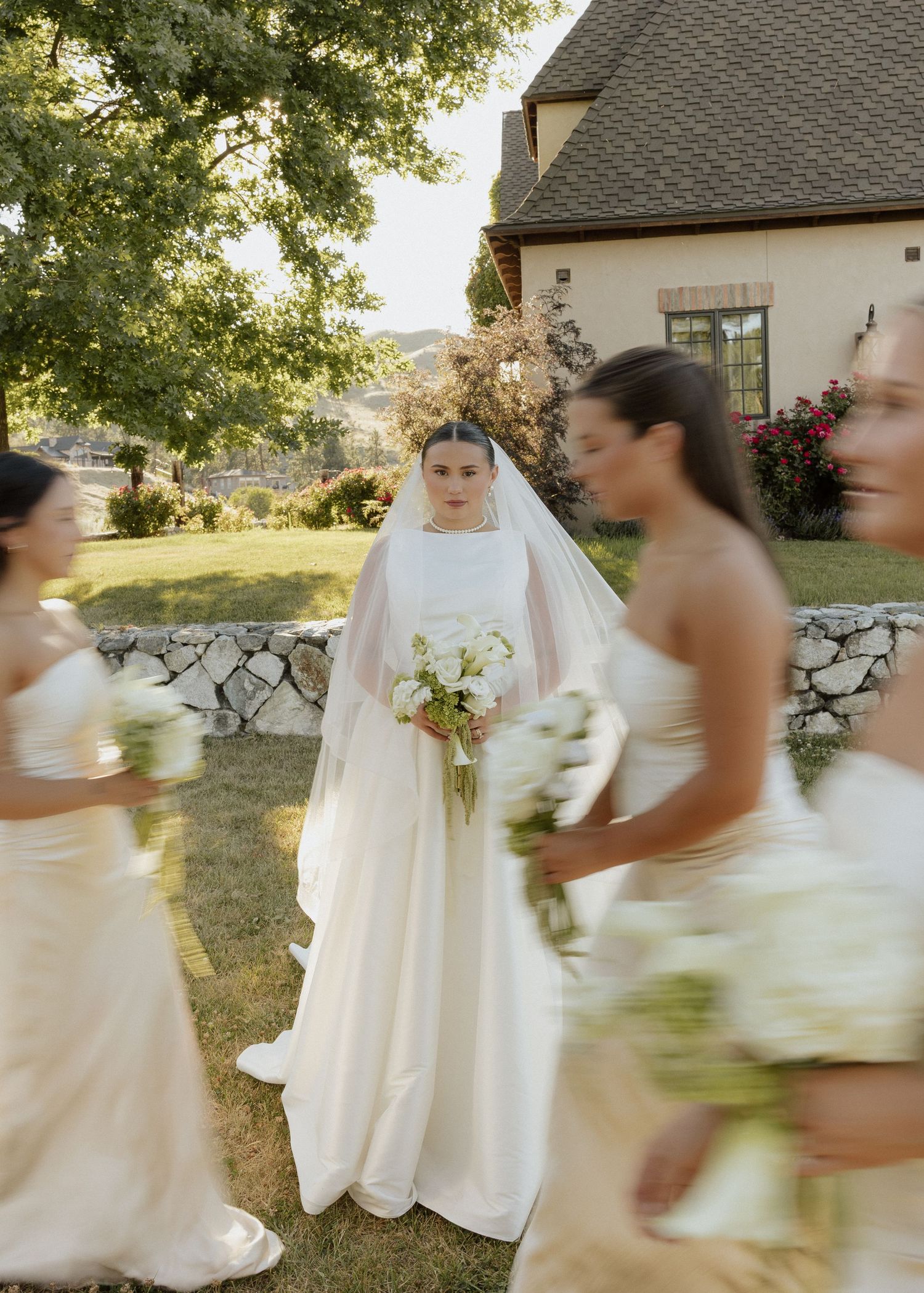 Bride in white gown and veil holding bouquet surrounded by bridesmaids in champagne dresses.