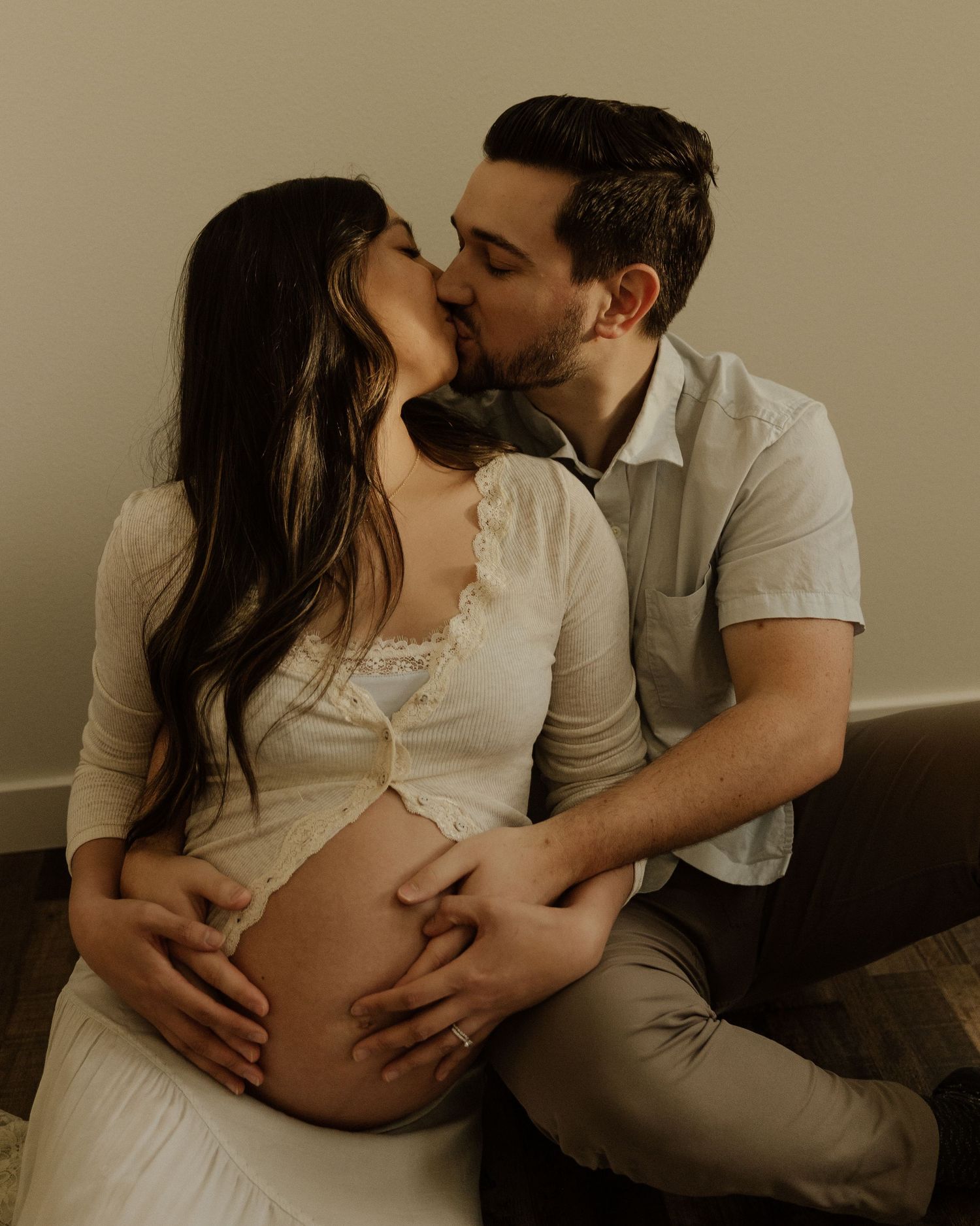 A couple share an intimate moment during a maternity photoshoot, with hands tenderly placed on the pregnant belly.