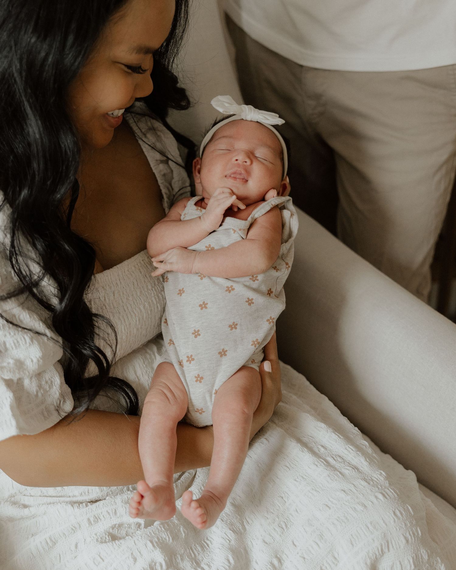 Joyful moment as newborn stretches while being held in white floral onesie.