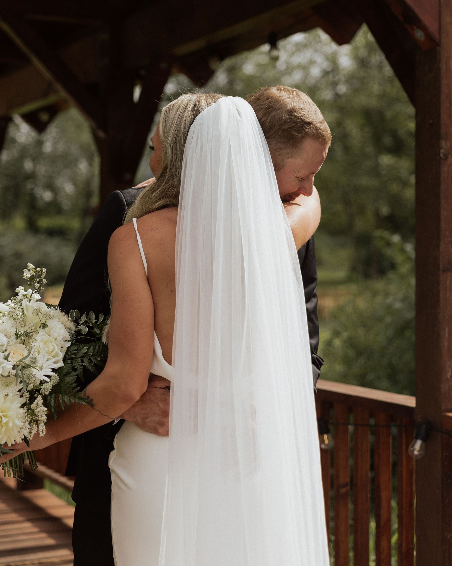 Intimate moment between newlyweds on a covered wooden bridge with white floral bouquet.