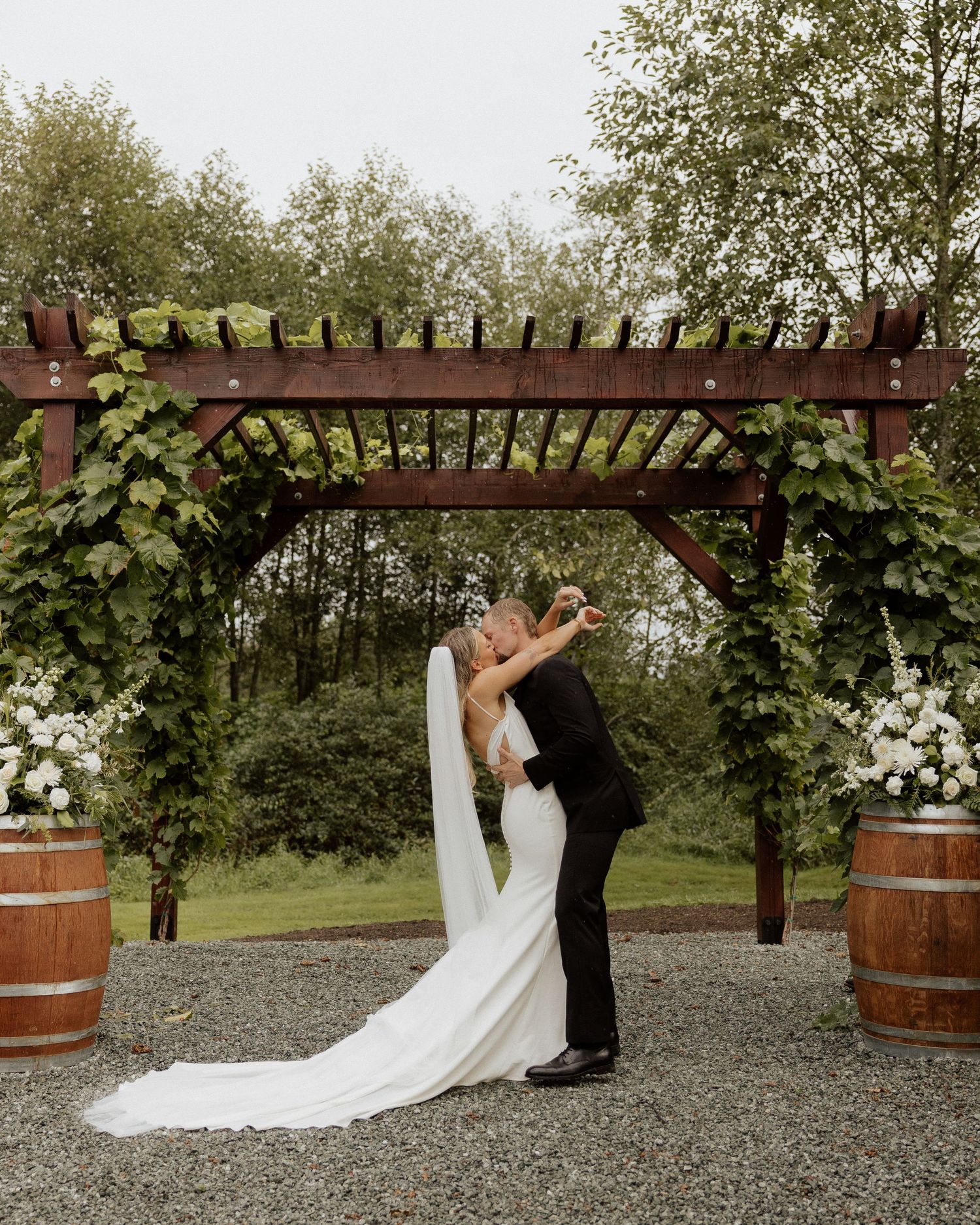 Wedding couple shares a tender moment beneath a vine-covered wooden arbor.