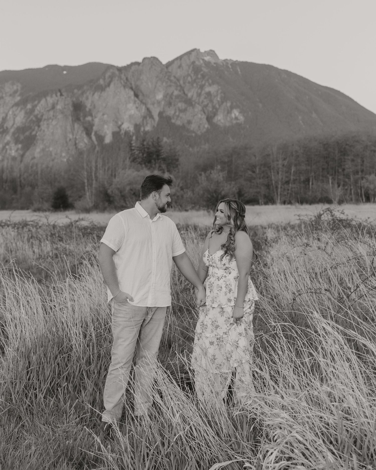 Black and white portrait of couple standing in field with mountain view.