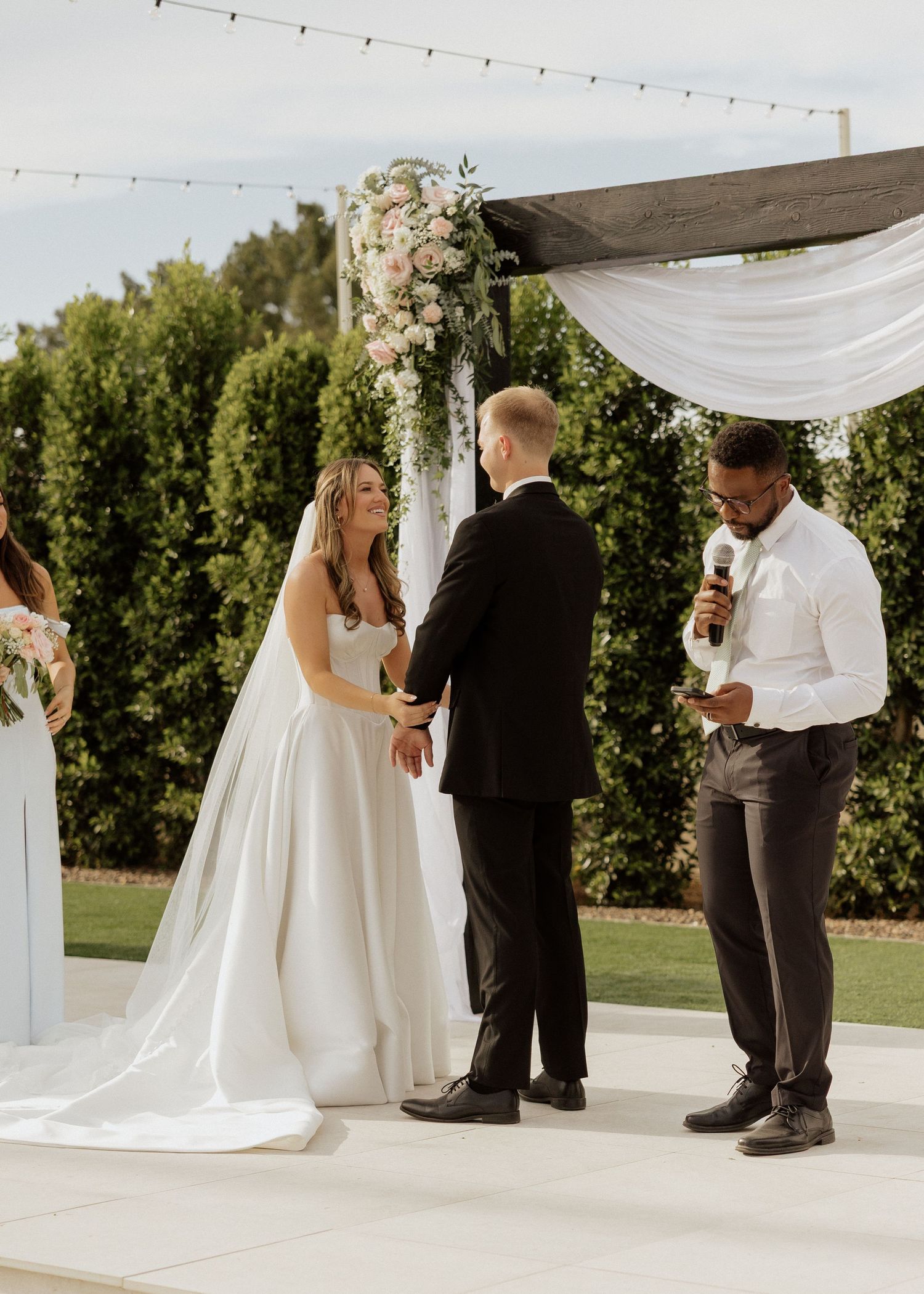Bride and groom holding hands at altar while officiant reads during outdoor wedding ceremony.