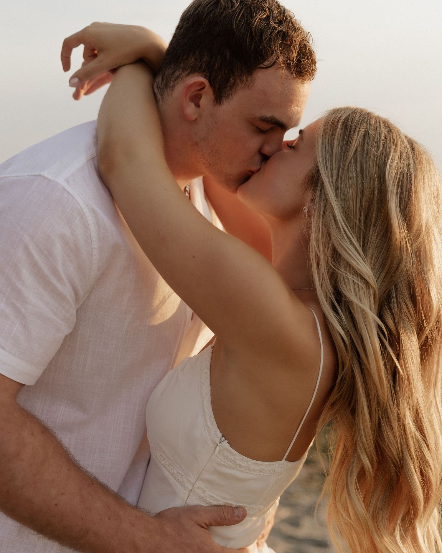 Intimate beachside portrait of couple sharing passionate kiss at sunset.