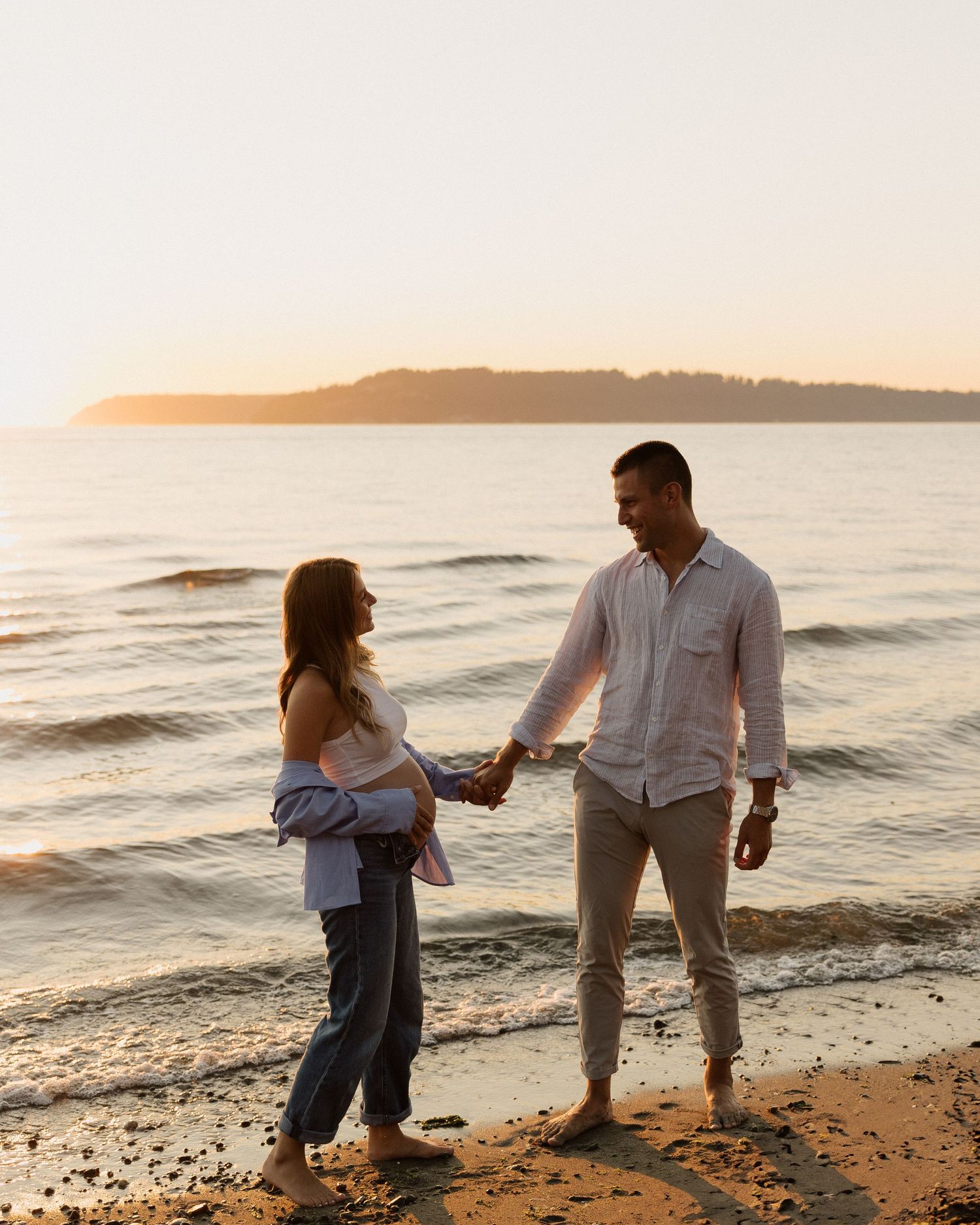 Couple standing together on sandy beach during golden hour sunset.
