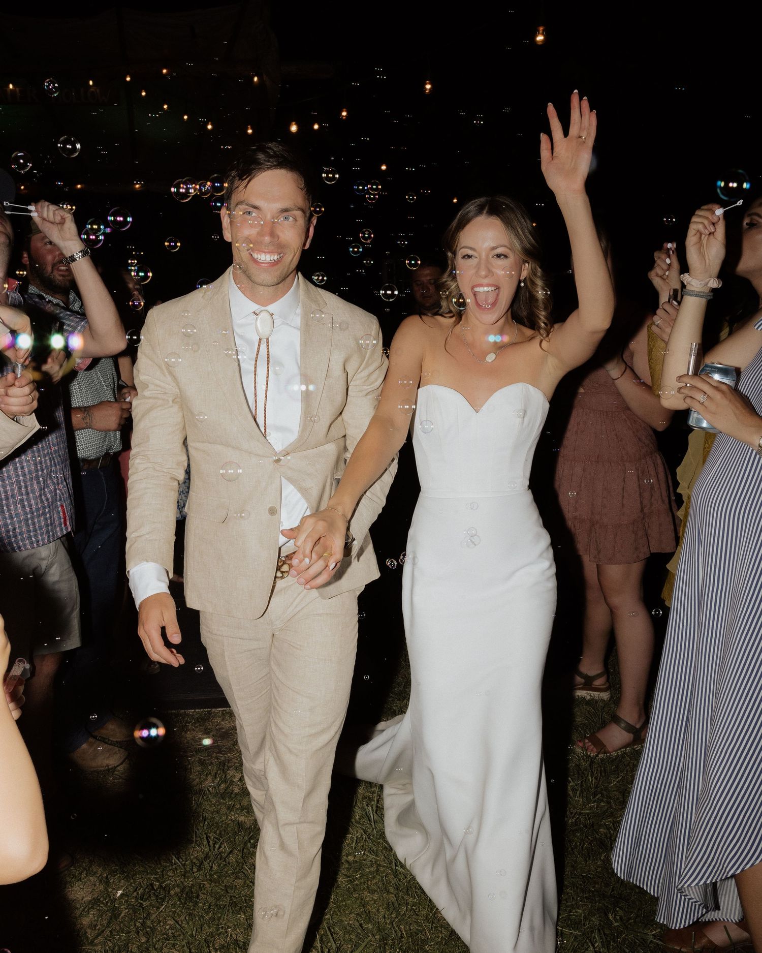 Joyful wedding couple celebrating with guests at nighttime outdoor reception.