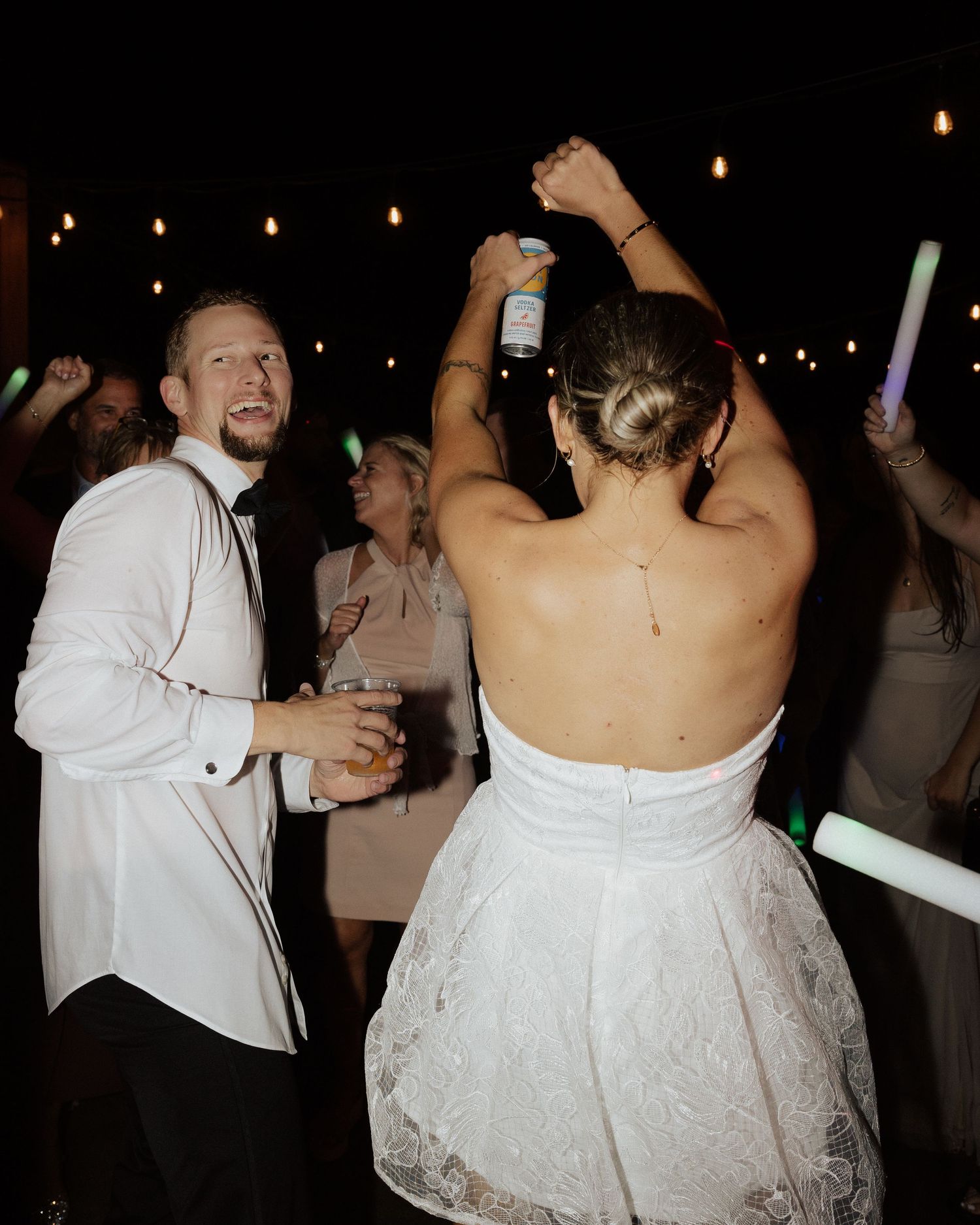 Party guests dancing and celebrating under string lights at an outdoor wedding reception.