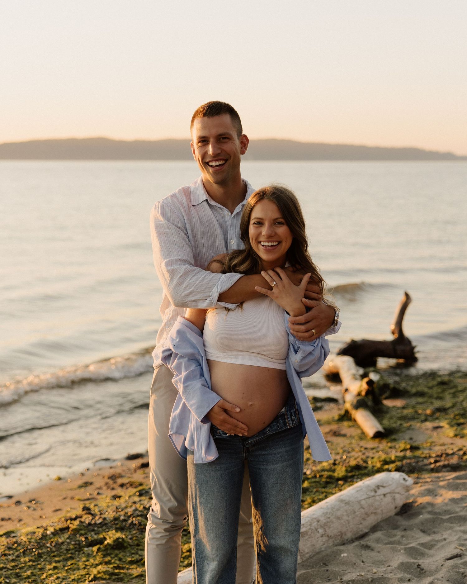 Joyful maternity moment captured on coastal beach at sunset.