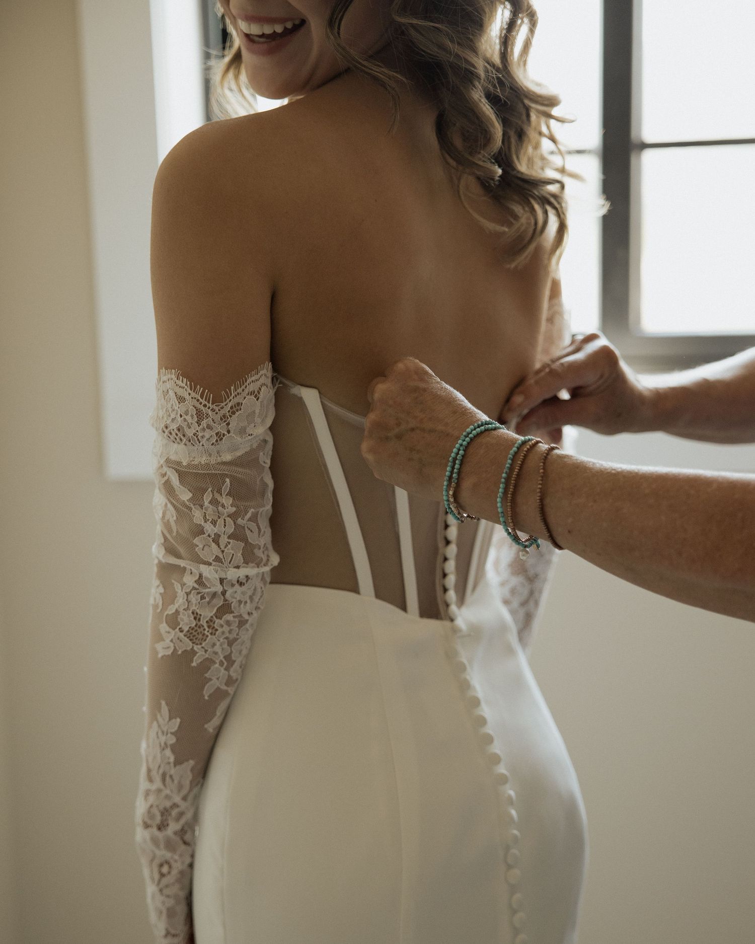 Close-up of intricate lace detailing on the back of a fitted wedding gown during final adjustments.