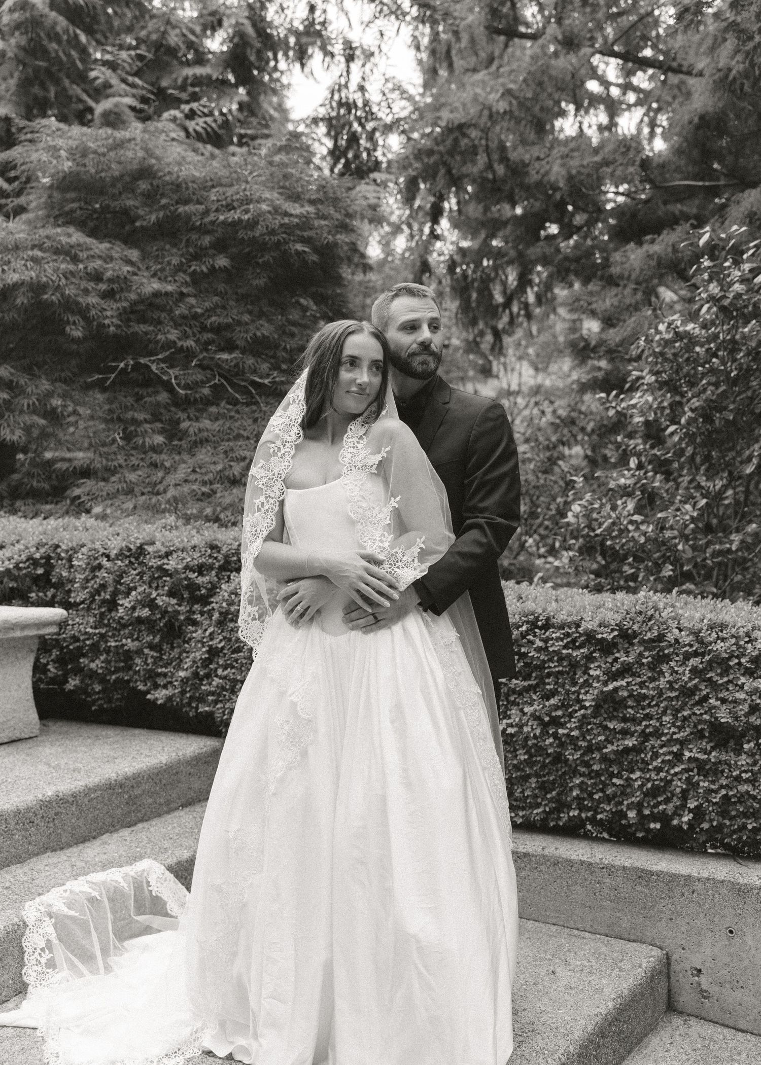 Bride and groom embracing in garden in classic black and white wedding portrait.