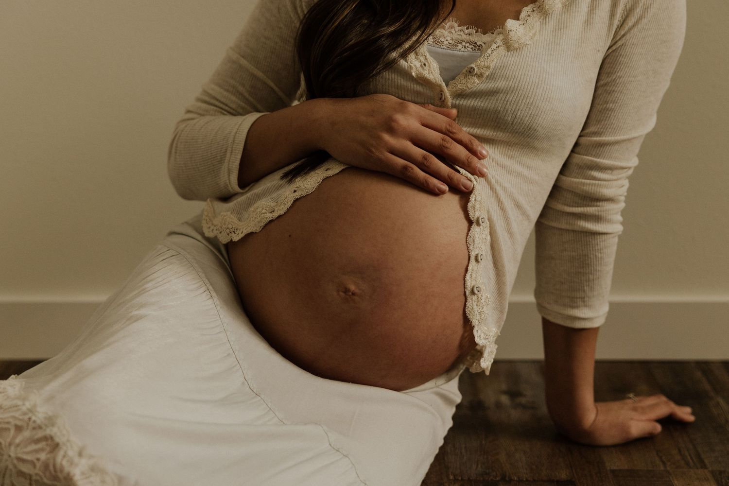 A serene maternity portrait featuring an expectant mother in white lace touching her belly.