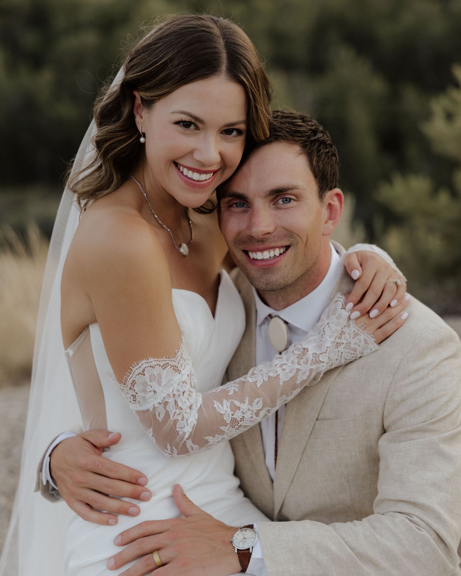 Close up portrait of newlyweds smiling together, bride wearing lace sleeve dress and flowing veil.