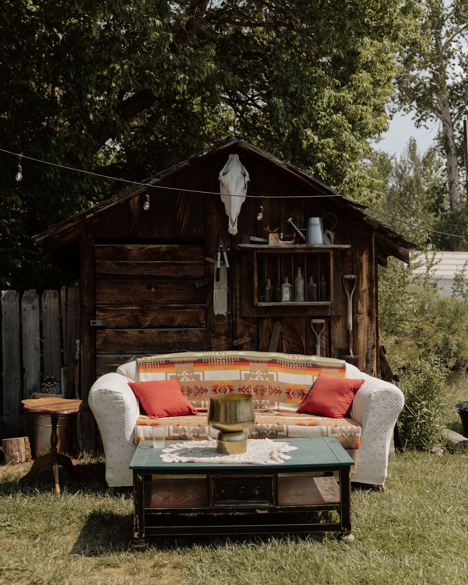 Vintage couch with red pillows against rustic wooden shed backdrop.