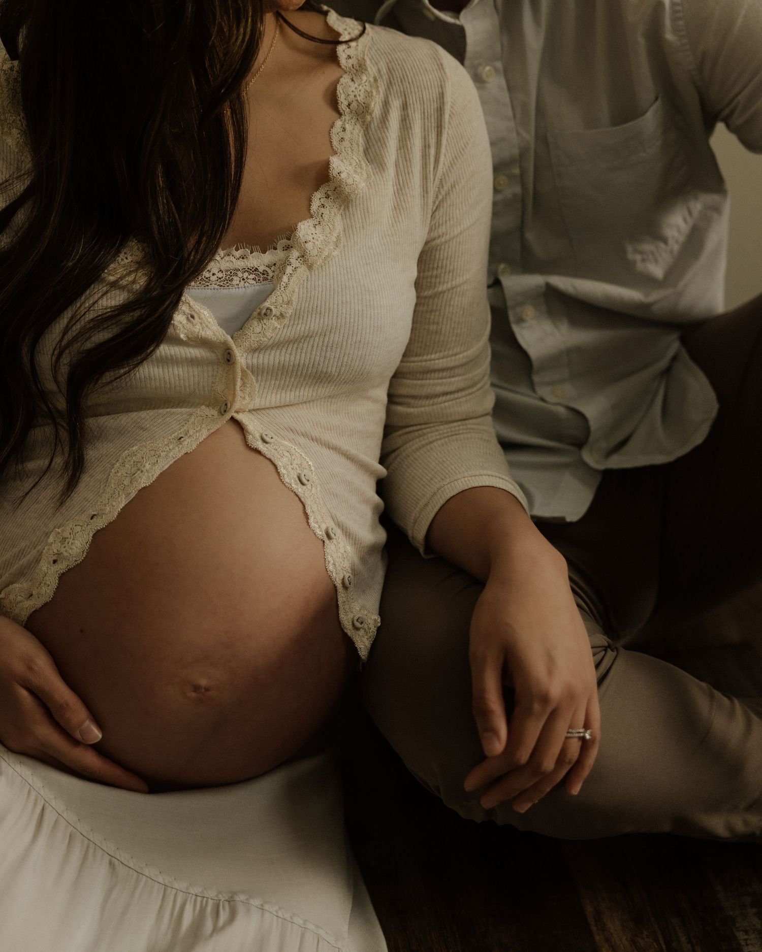 An intimate maternity photo showing a pregnant belly in a cream-colored lace top.